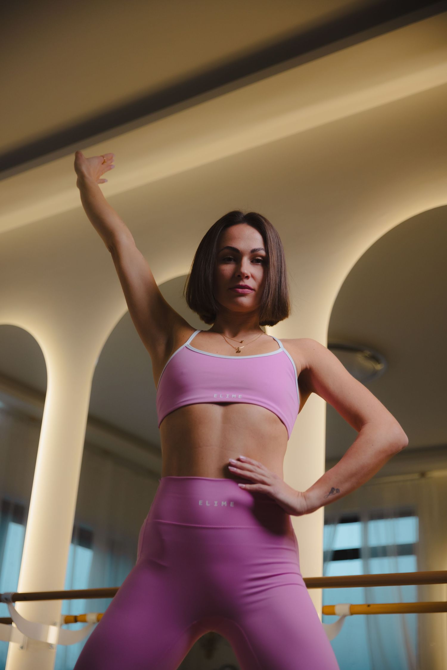 Dancer in purple athletic wear practicing movements at a ballet studio with natural lighting.