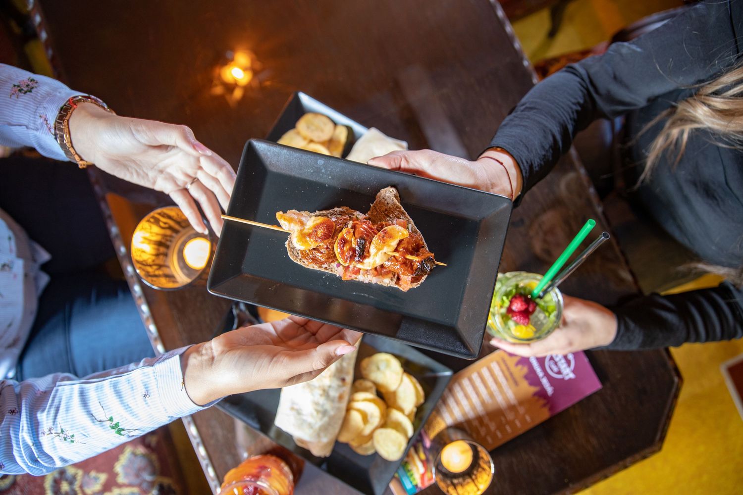 Overhead view of multiple hands reaching for food and drinks across a restaurant table.