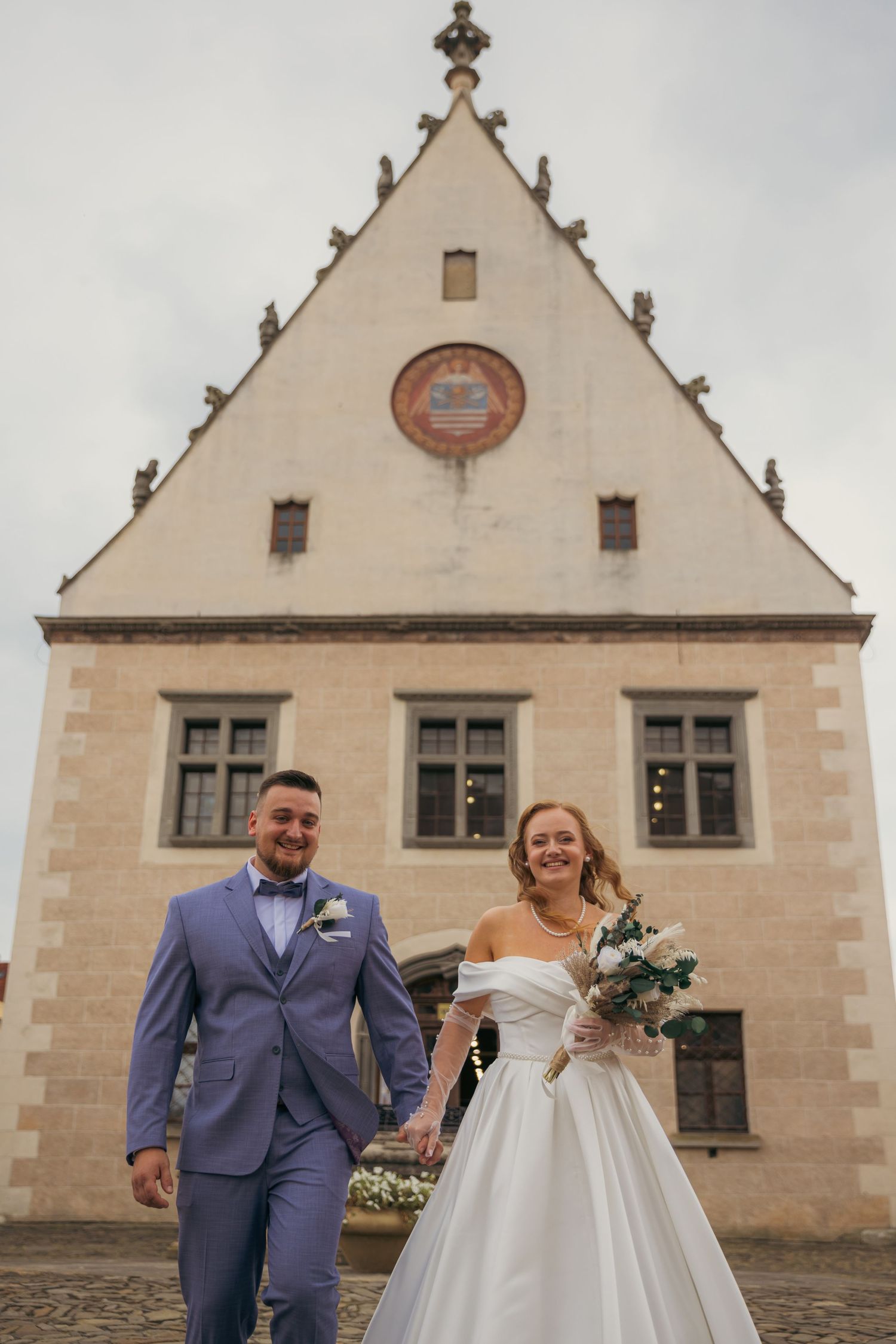 Newlyweds walking together outside historic stone church building.