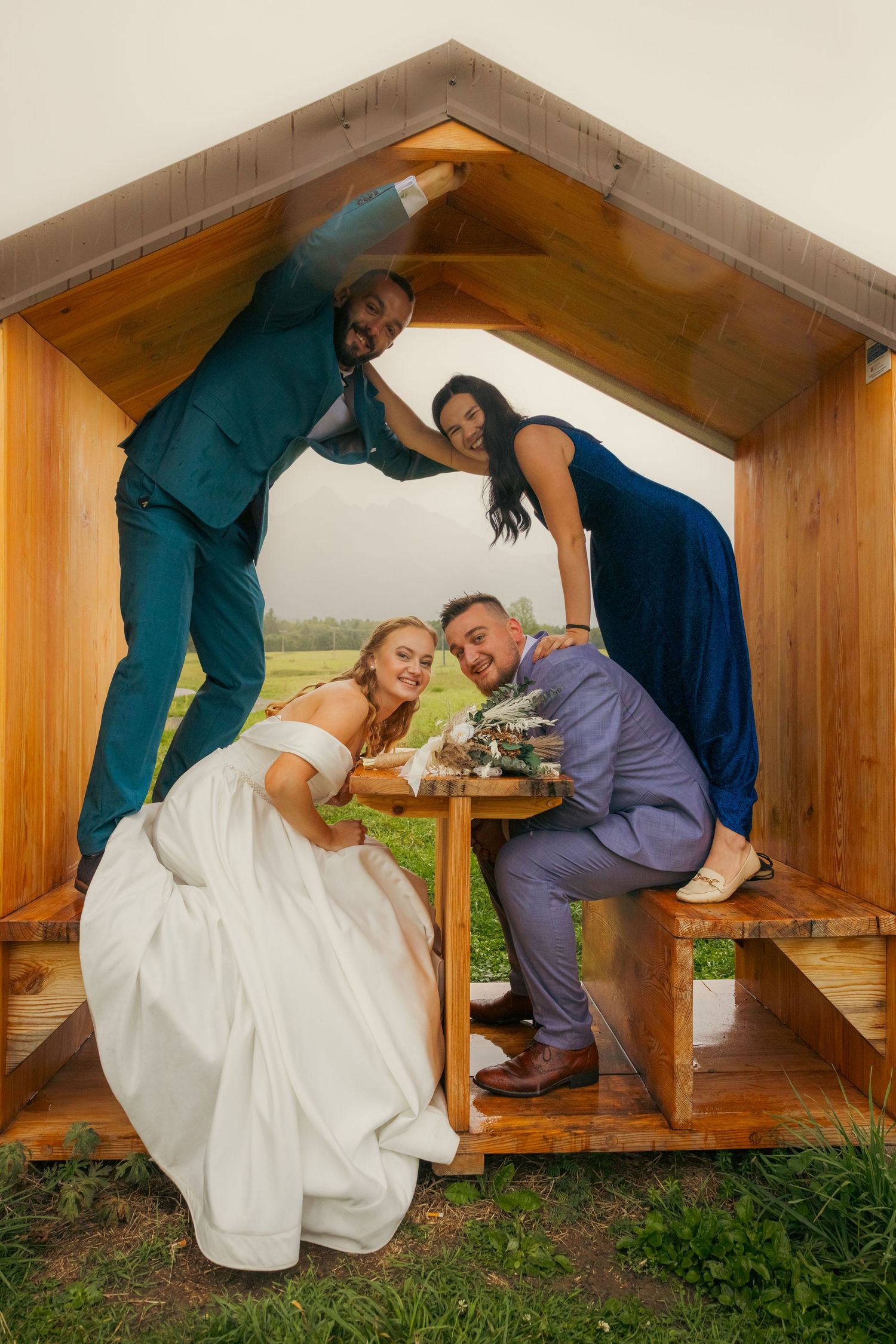 Playful wedding couple posing under wooden shelter in countryside.