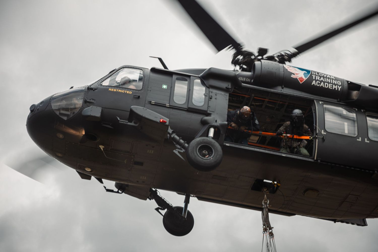 Black military helicopters in formation flying against overcast sky during emergency response mission.
