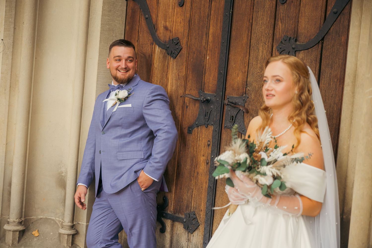 Wedding couple posing against wooden door of historic building.