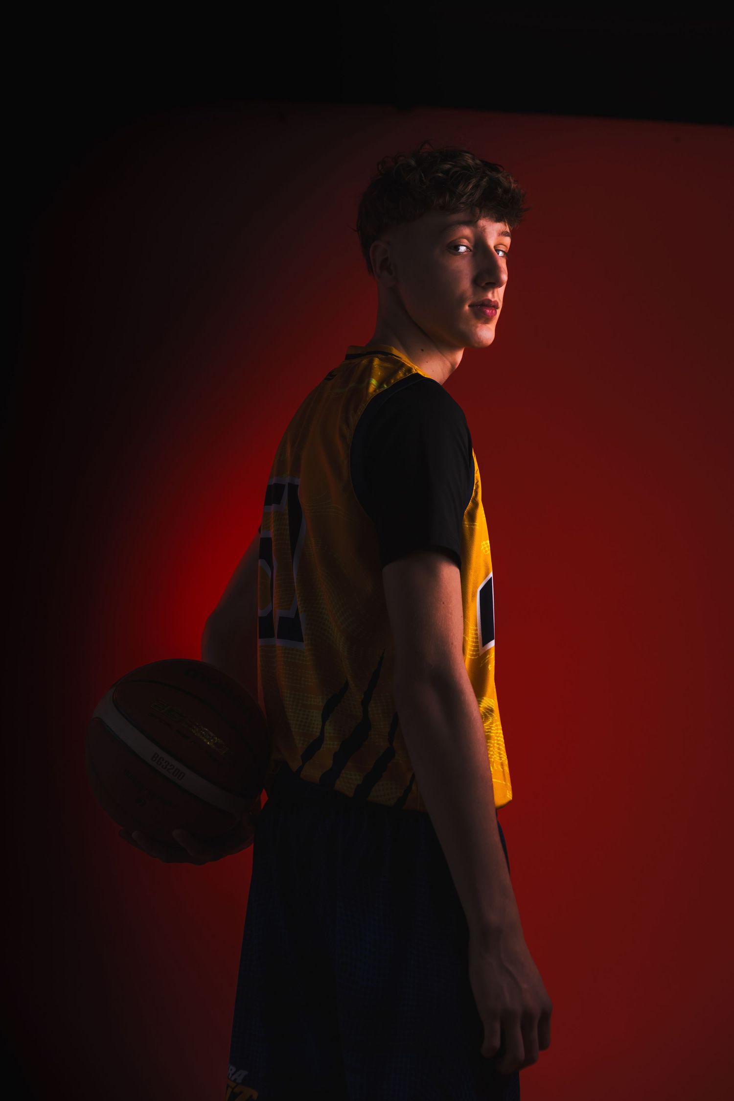 Basketball player in navy uniform poses against dramatic red background.