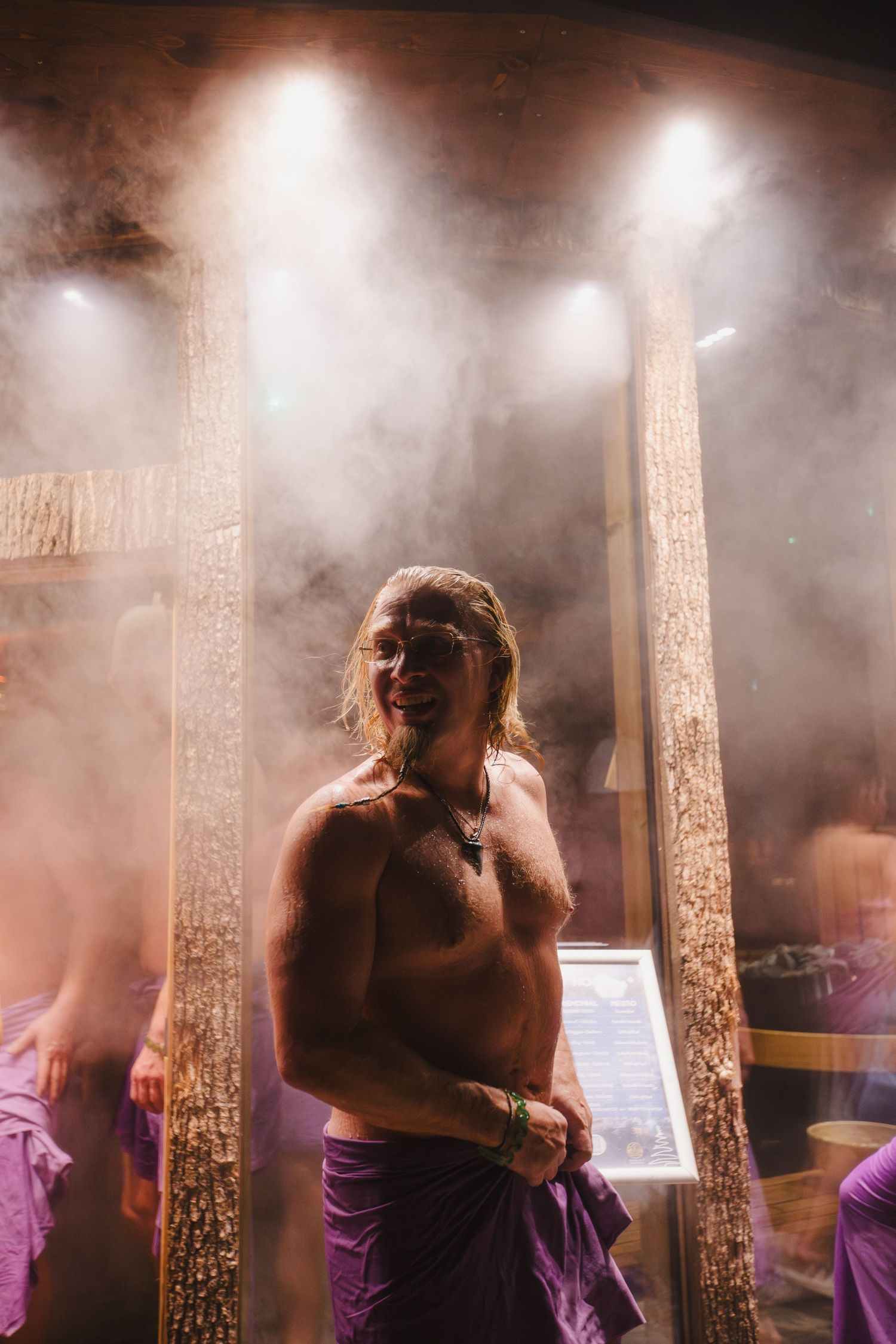 Performers in purple costumes stand amidst atmospheric stage fog and dramatic lighting during a show.