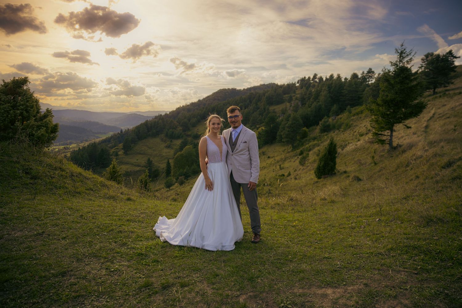 A couple shares a romantic moment against a dramatic mountain sunset landscape.