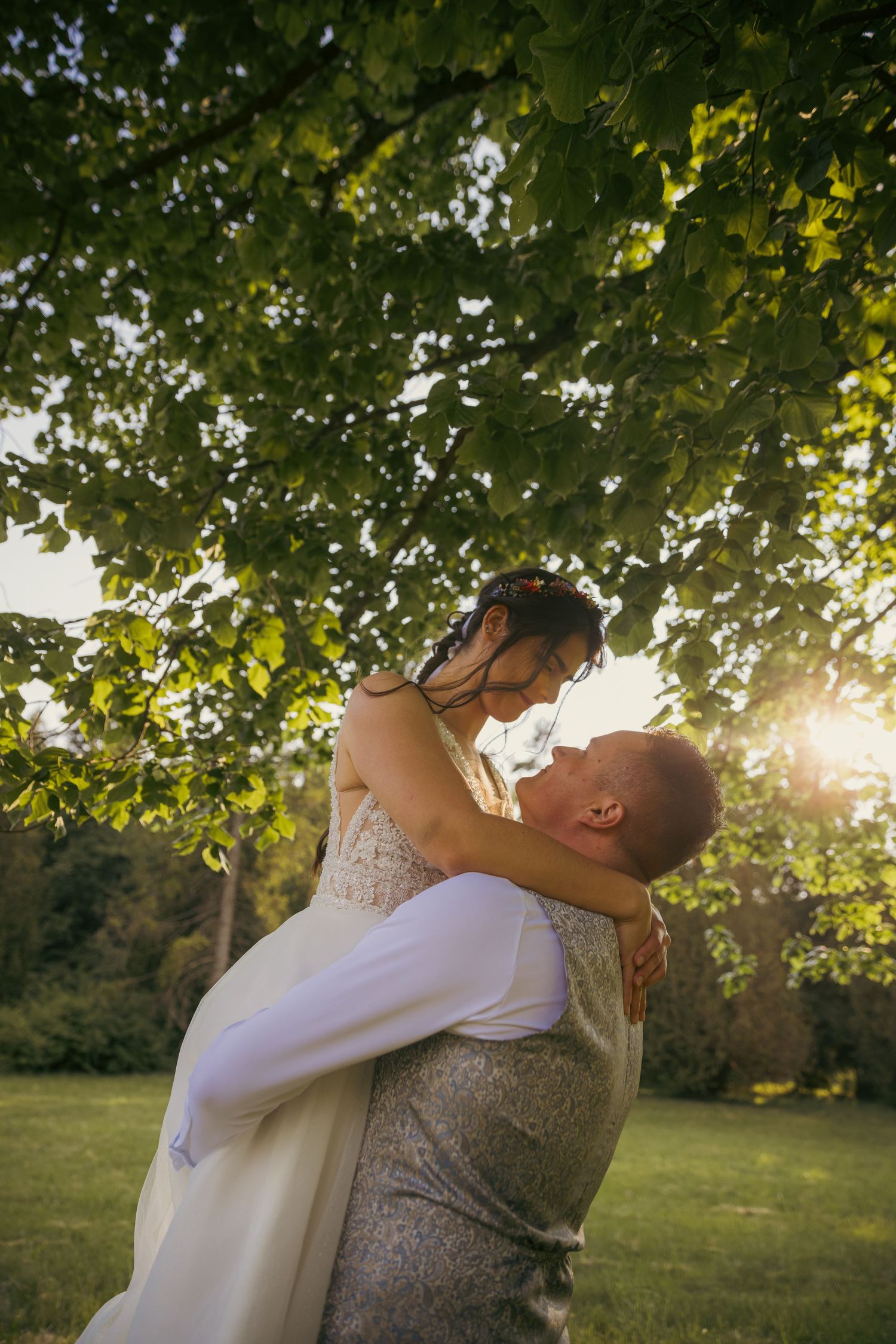 Romantic sunset wedding photo of couple embracing under tree branches with golden sunlight filtering through leaves.