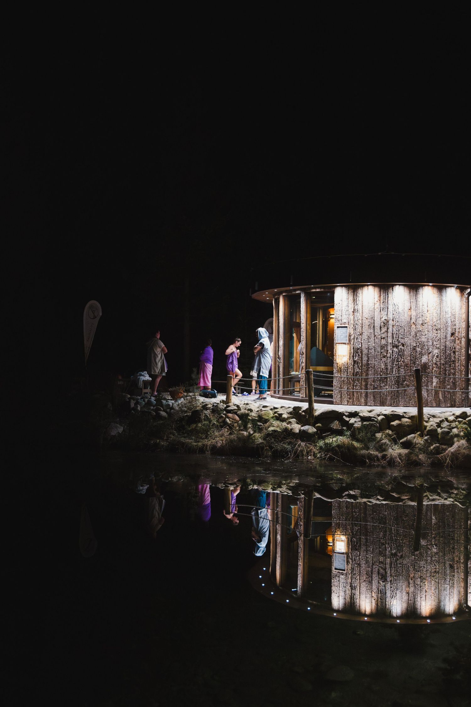 Nighttime nativity scene display reflected in water with illuminated figures and structures.