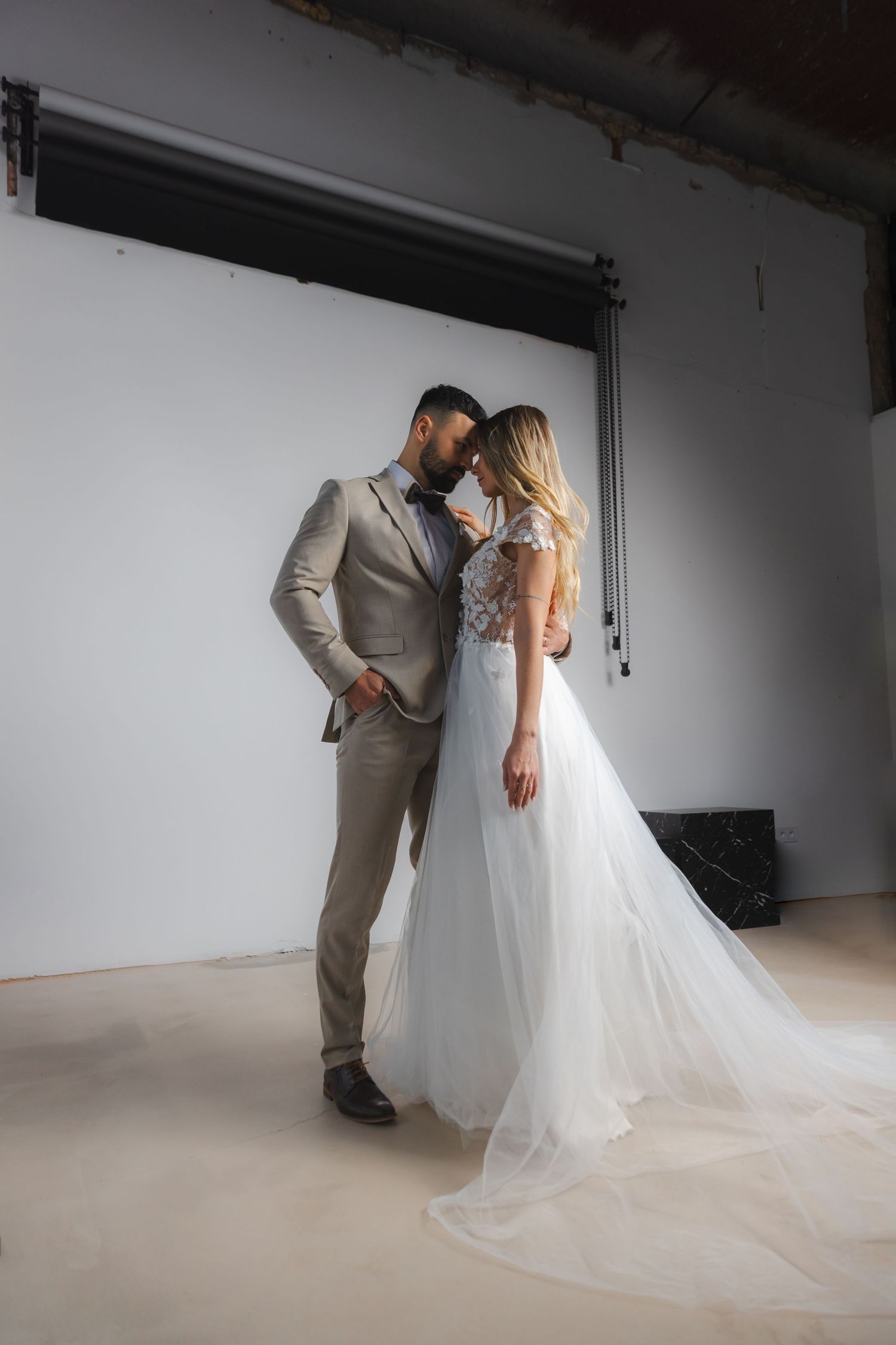 Couple in wedding attire share intimate moment in studio setting.
