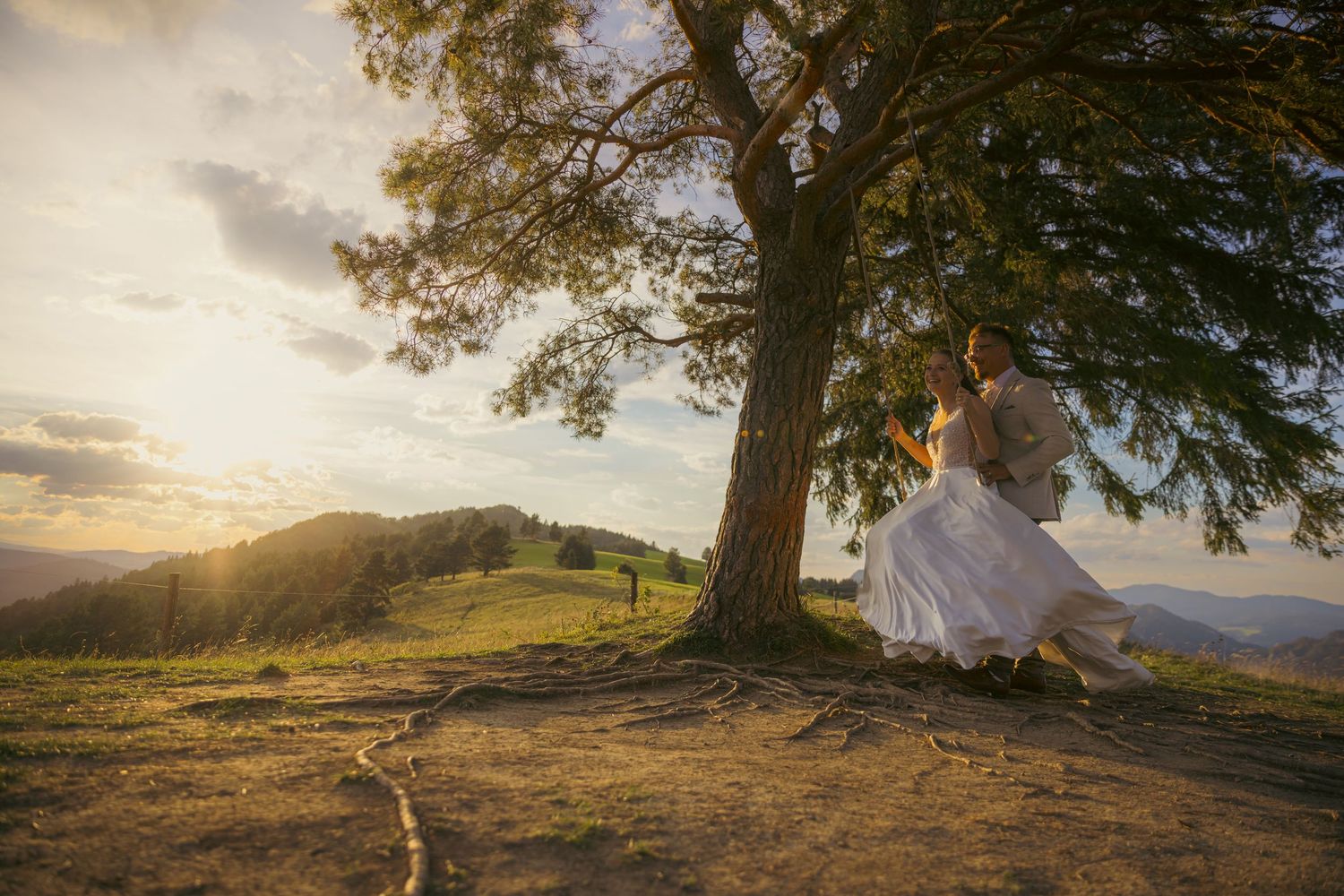 Wedding photography under a majestic tree with mountain vistas at sunset.