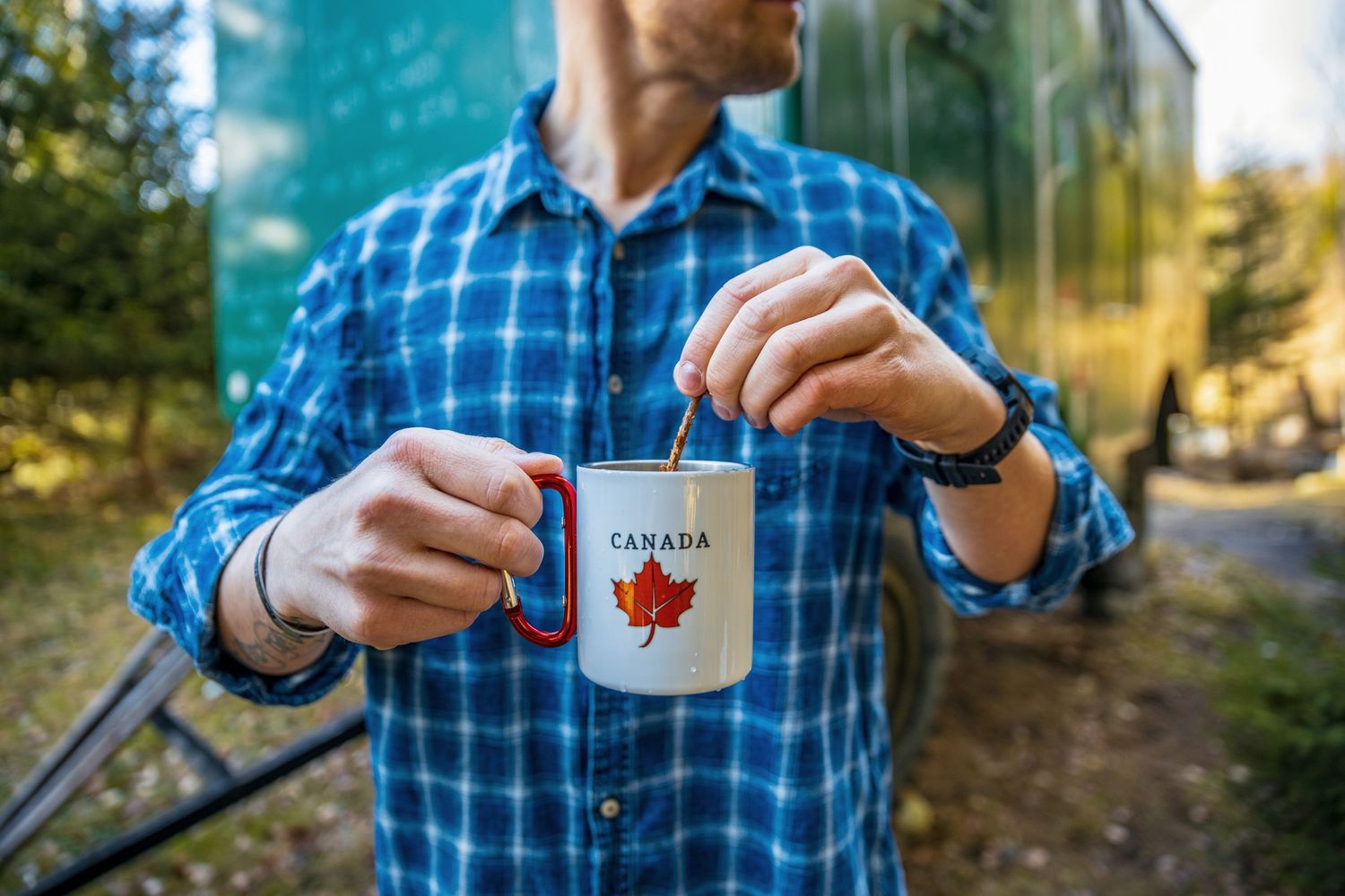 Person in blue plaid shirt enjoying coffee outdoors in natural setting.