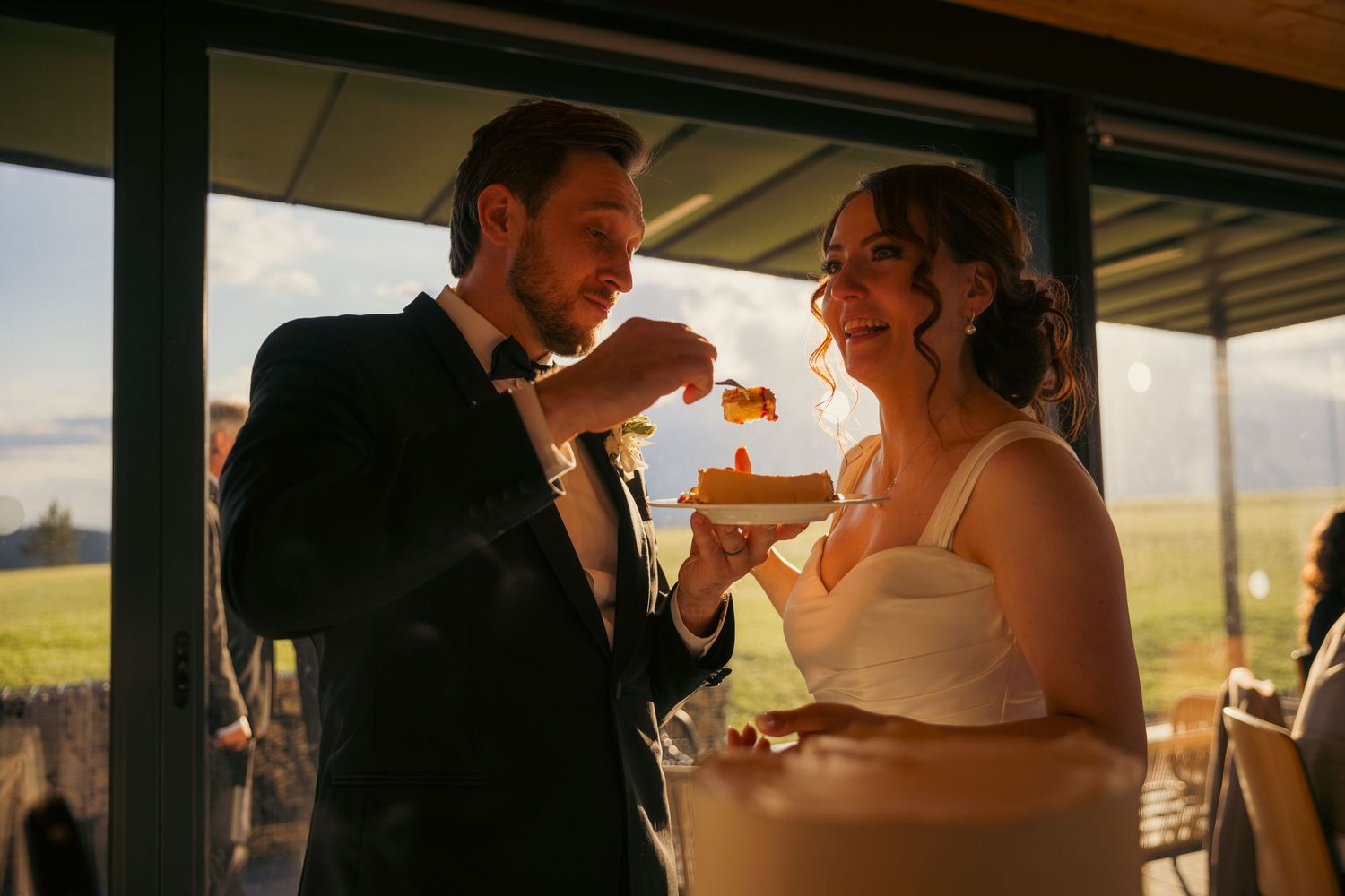 Silhouetted wedding couple sharing an intimate moment at sunset through window.