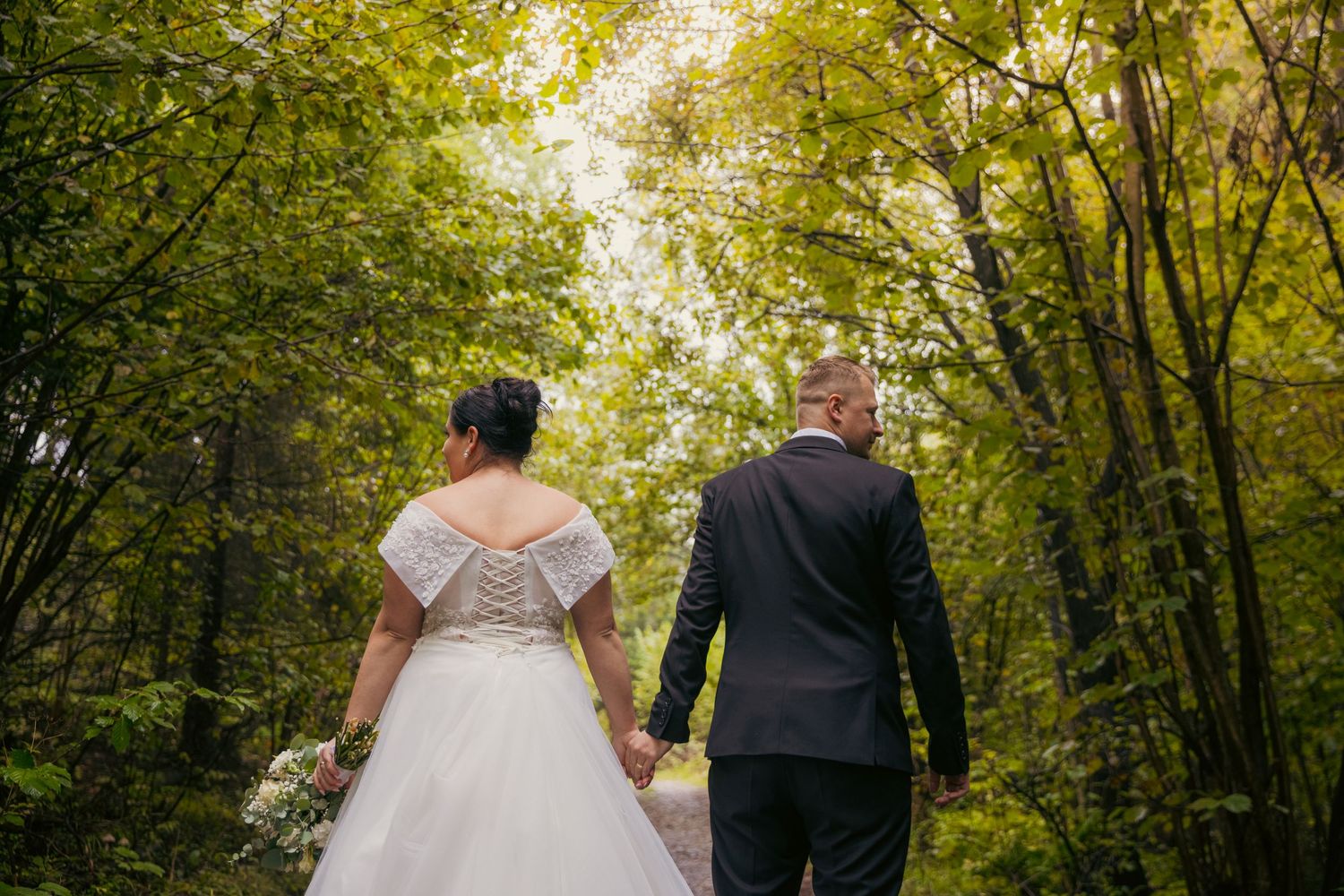 Newlyweds walk through a lush green forest path during golden hour.