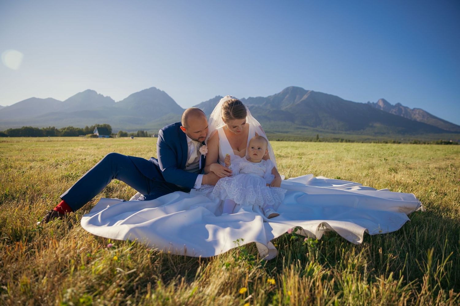 Wedding couple lies in mountain meadow with dramatic mountain peaks in background.