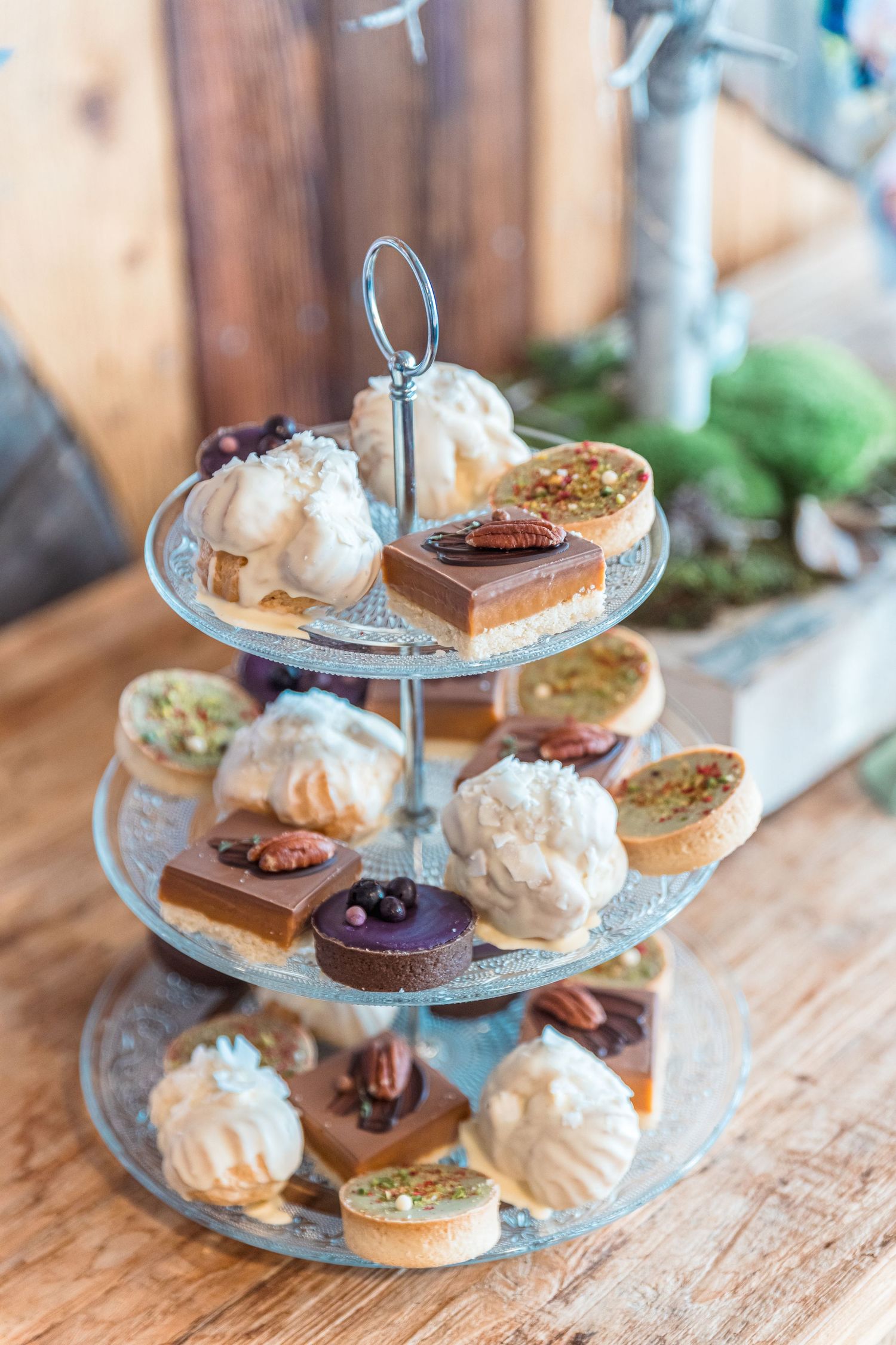 Three-tiered dessert stand displaying an assortment of gourmet pastries and sweets on wooden table.
