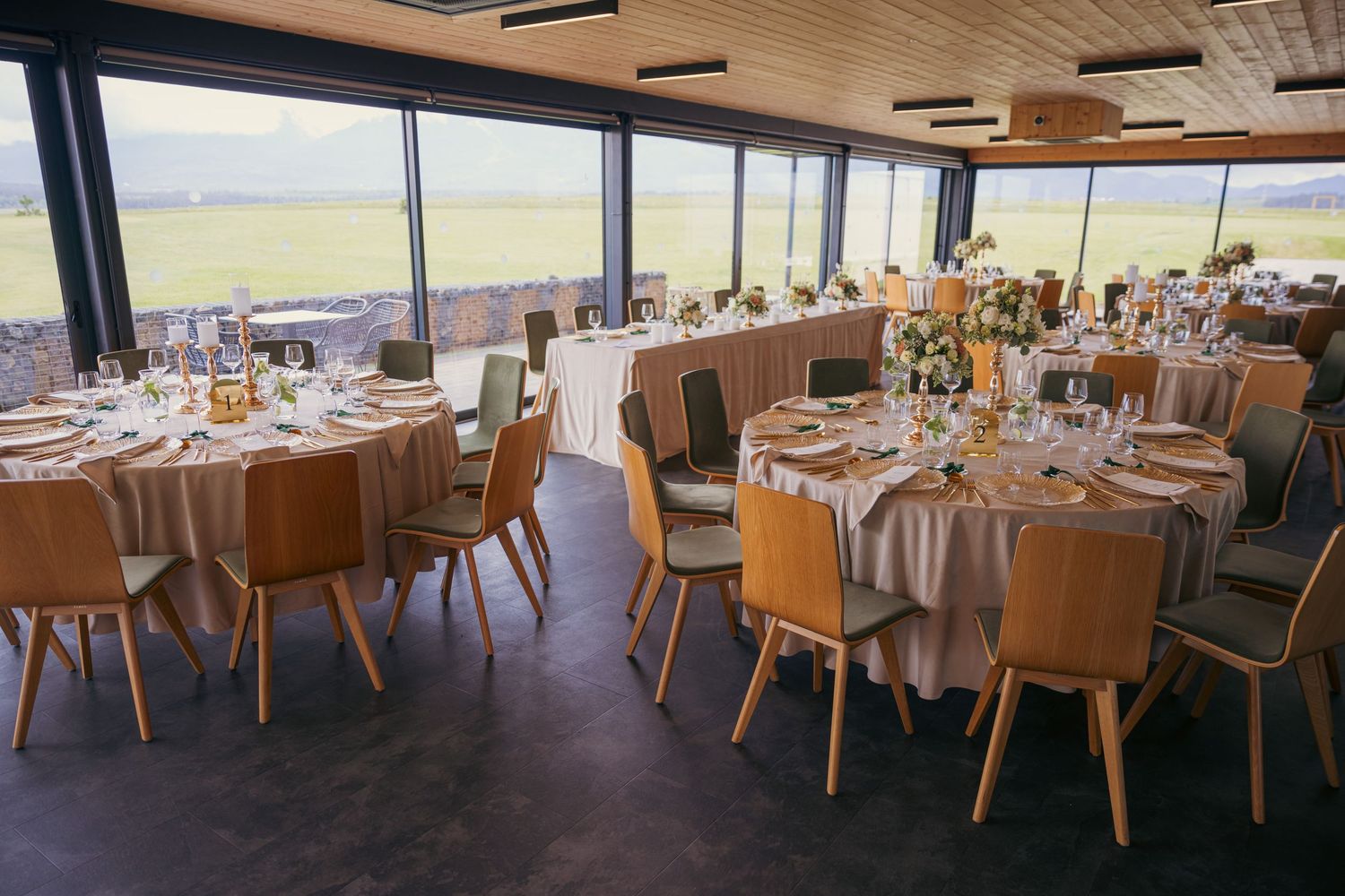 Panoramic view of wedding reception venue with round tables and wooden chairs.
