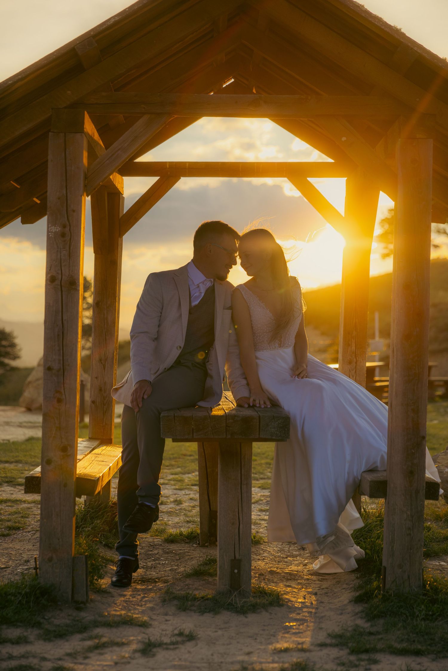 Golden sunlight streams through wooden shelter during intimate wedding moment.
