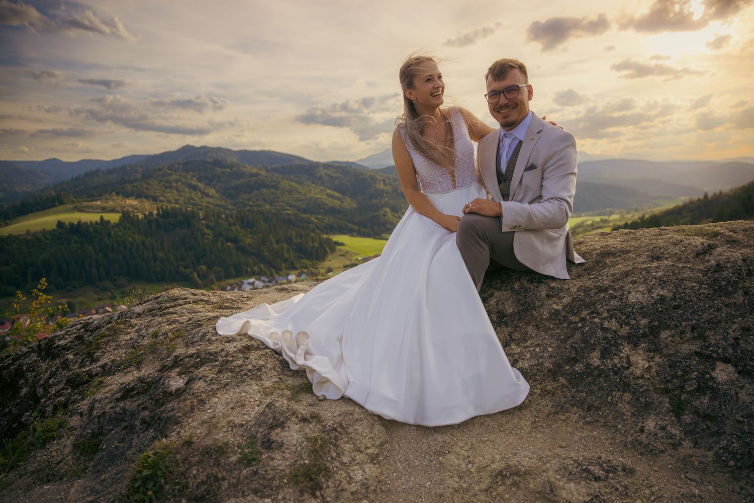 A couple stands on a hilltop overlook with sweeping mountain views at sunset.