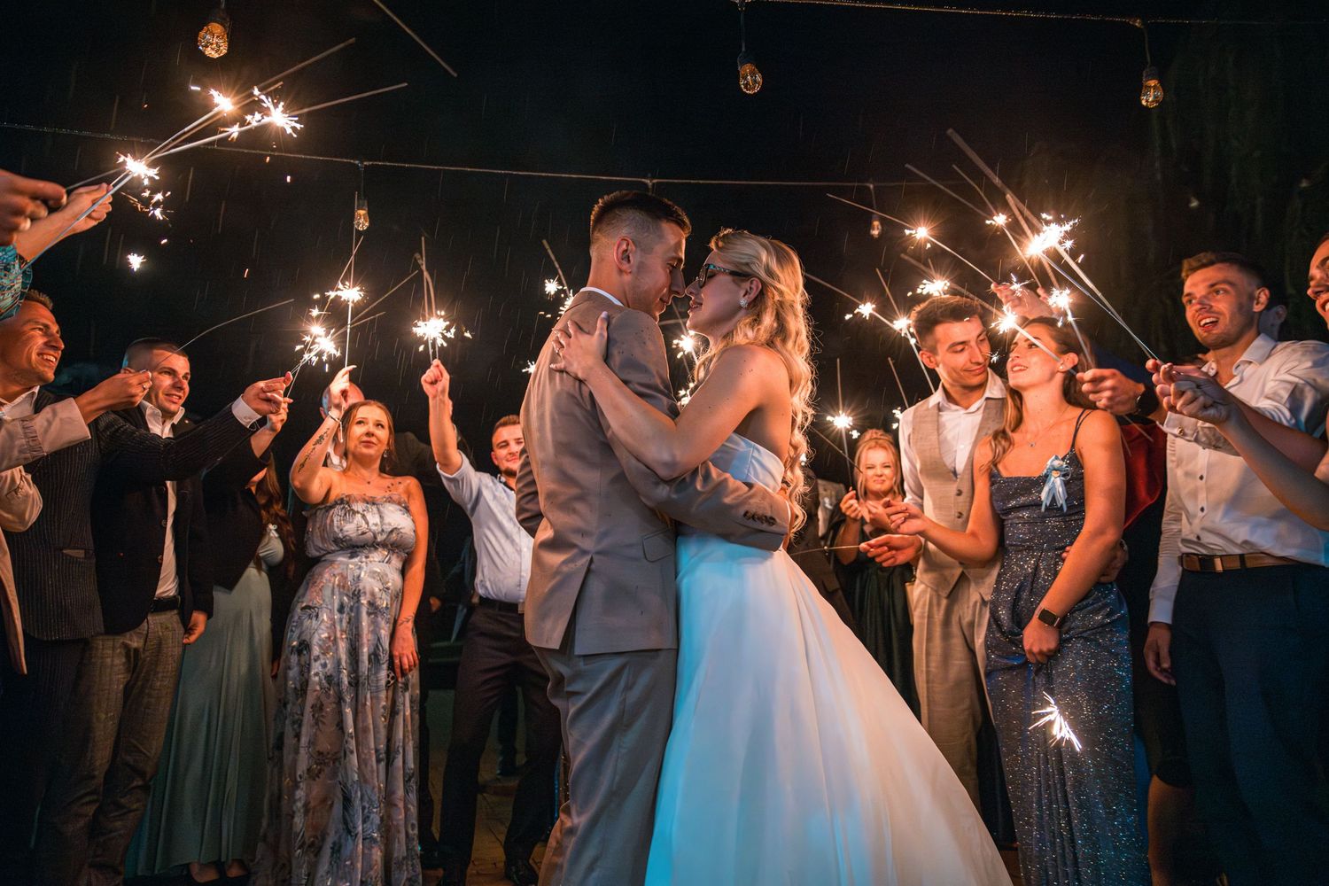 Wedding guests create a sparkler tunnel exit for the celebrating couple at night.