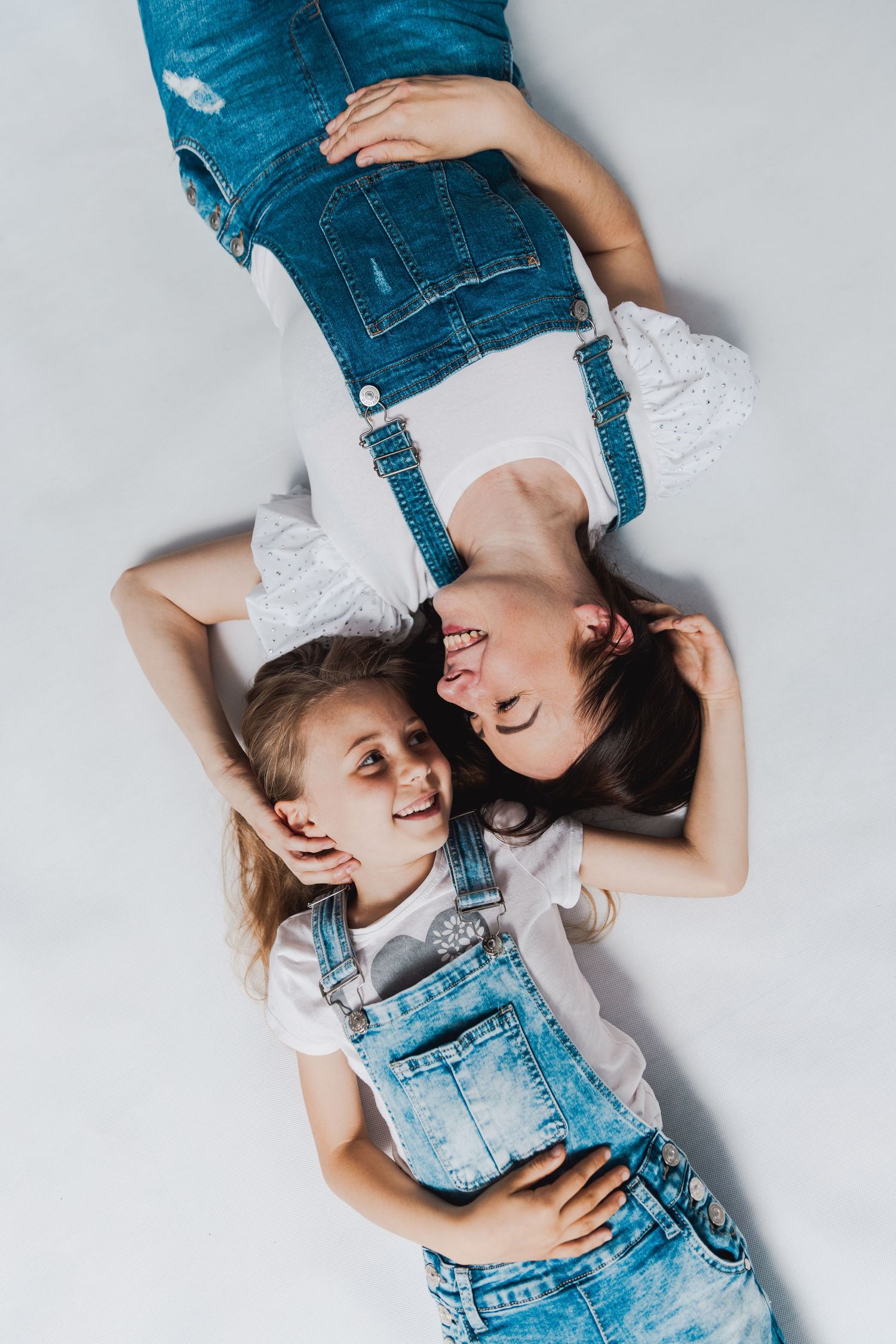 Two people wearing denim lie on a white background sharing joyful laughter together.