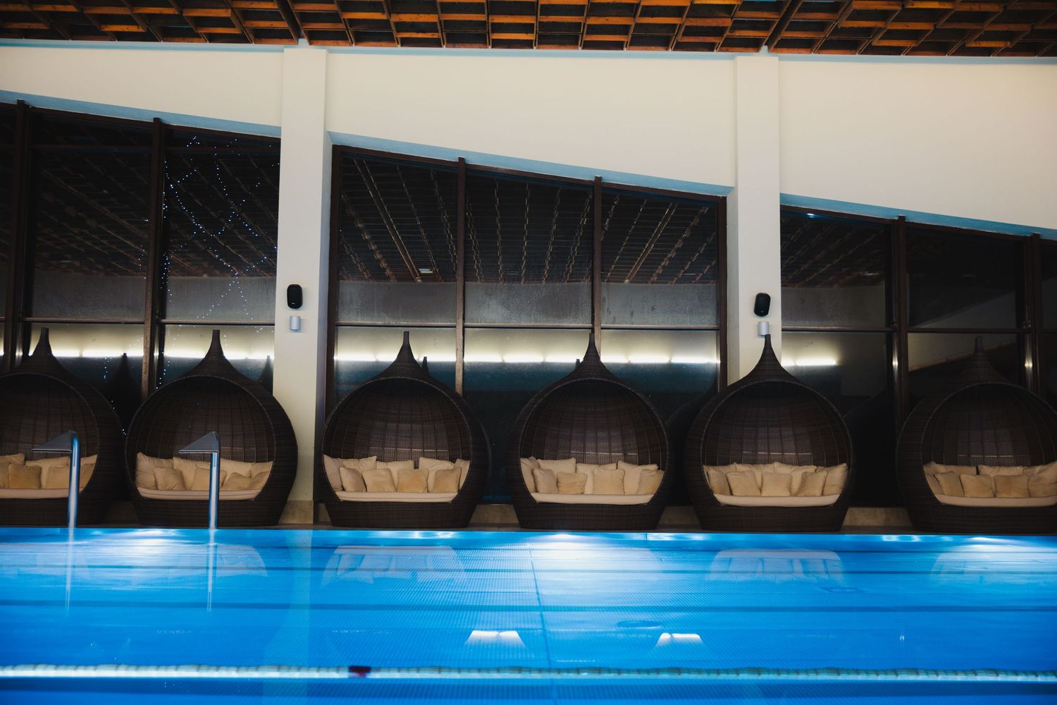 Row of hanging basket seats above blue swimming pool in modern indoor facility.