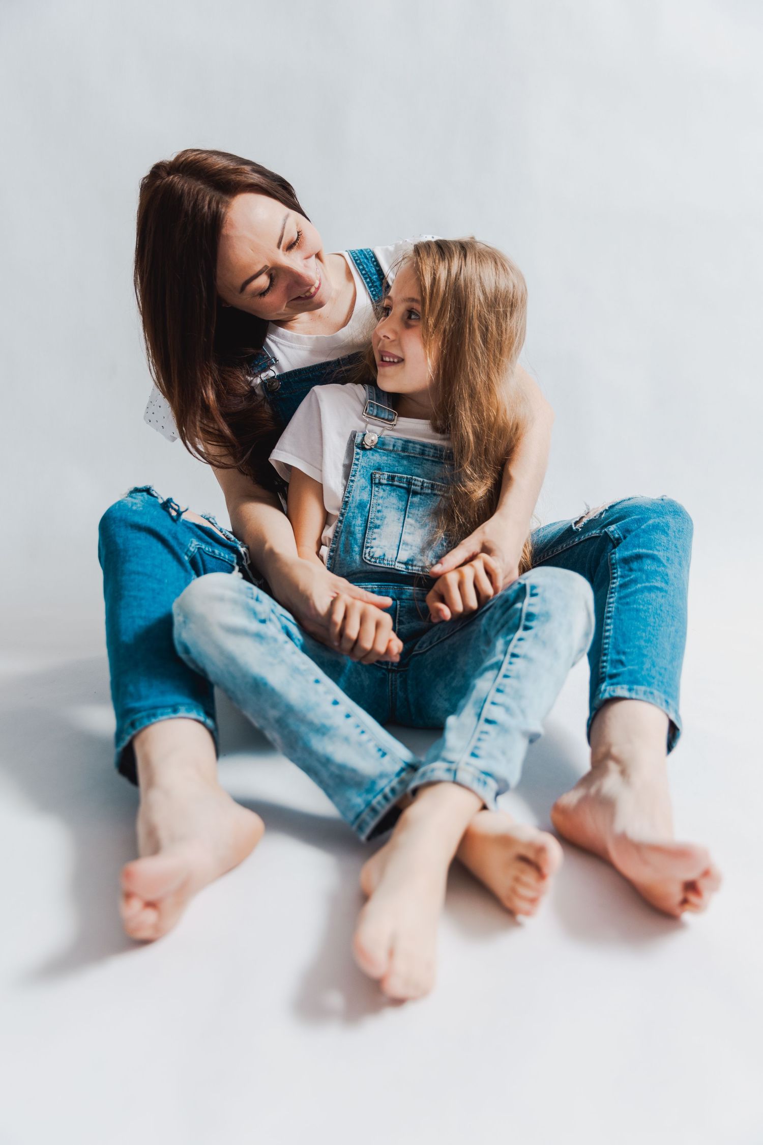 Two people in denim and white shirts sitting together on white background.