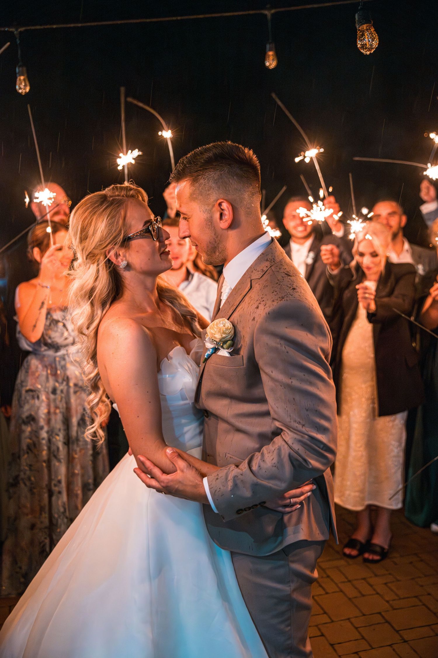 Newlyweds share a romantic dance surrounded by guests holding sparklers at night.