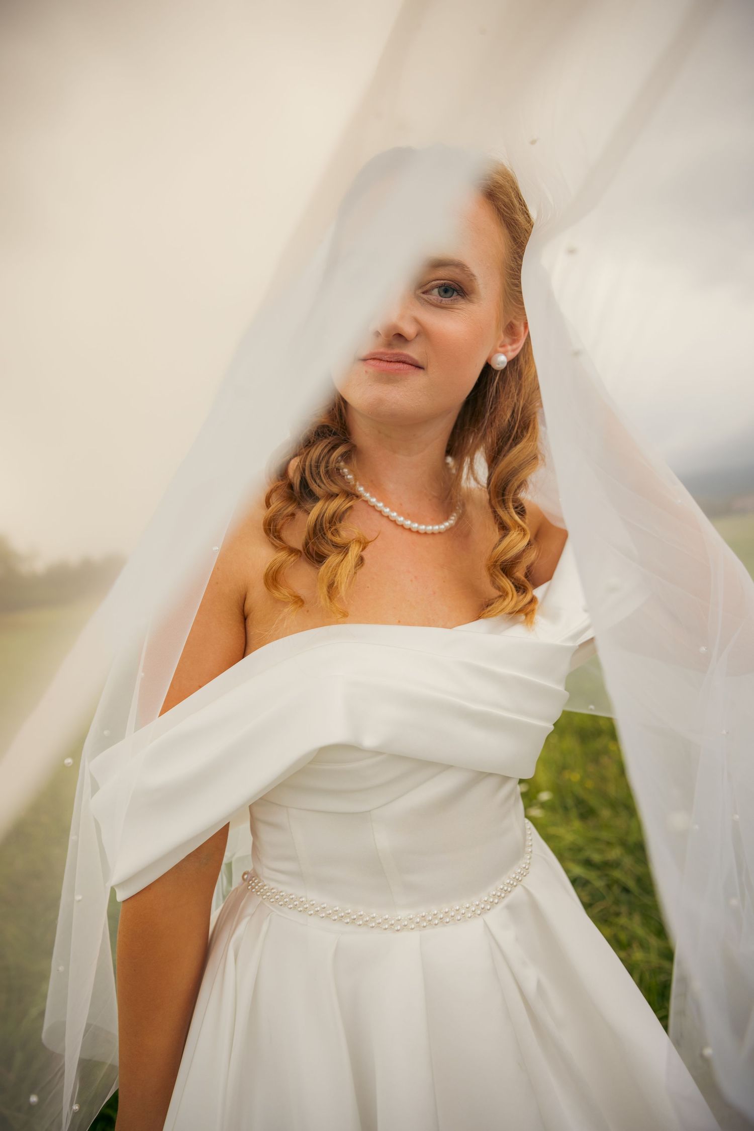 Close-up details of bride wearing white dress and pearl necklace with flowing veil.