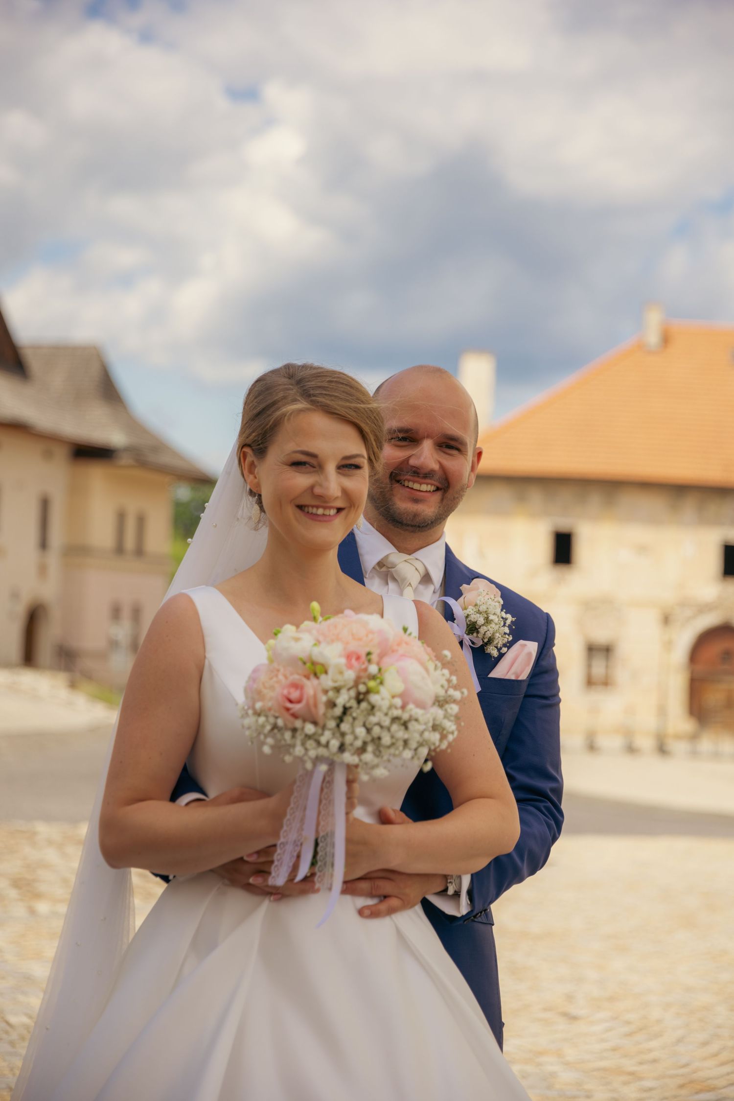 Bride and groom share joyful moments in front of historic stone buildings.