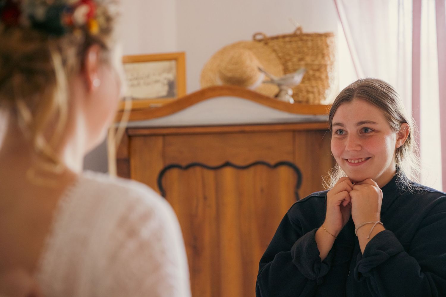 Intimate getting ready moment captured in warm bedroom setting with natural light.