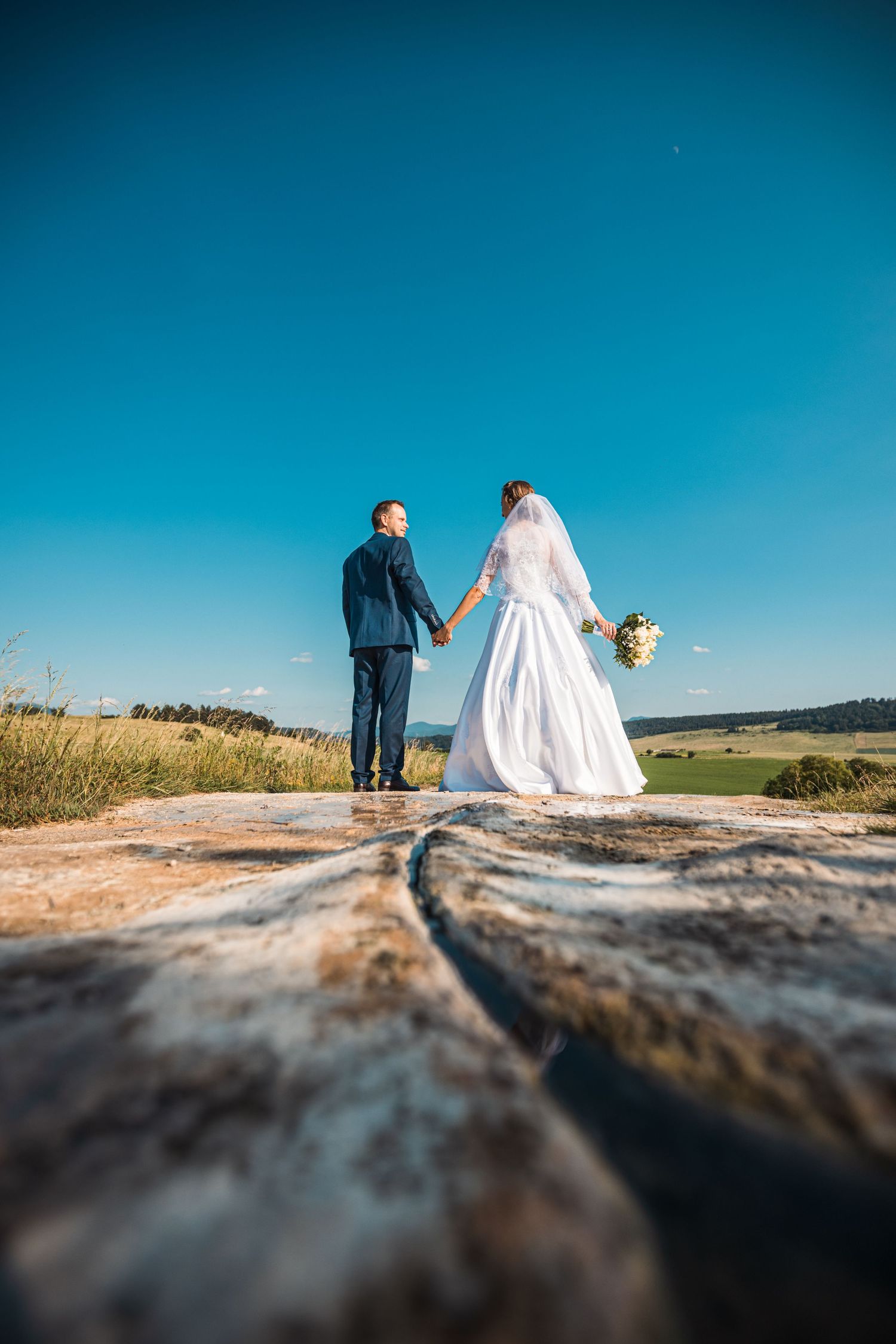 Wedding couple silhouetted against blue sky on rocky terrain.