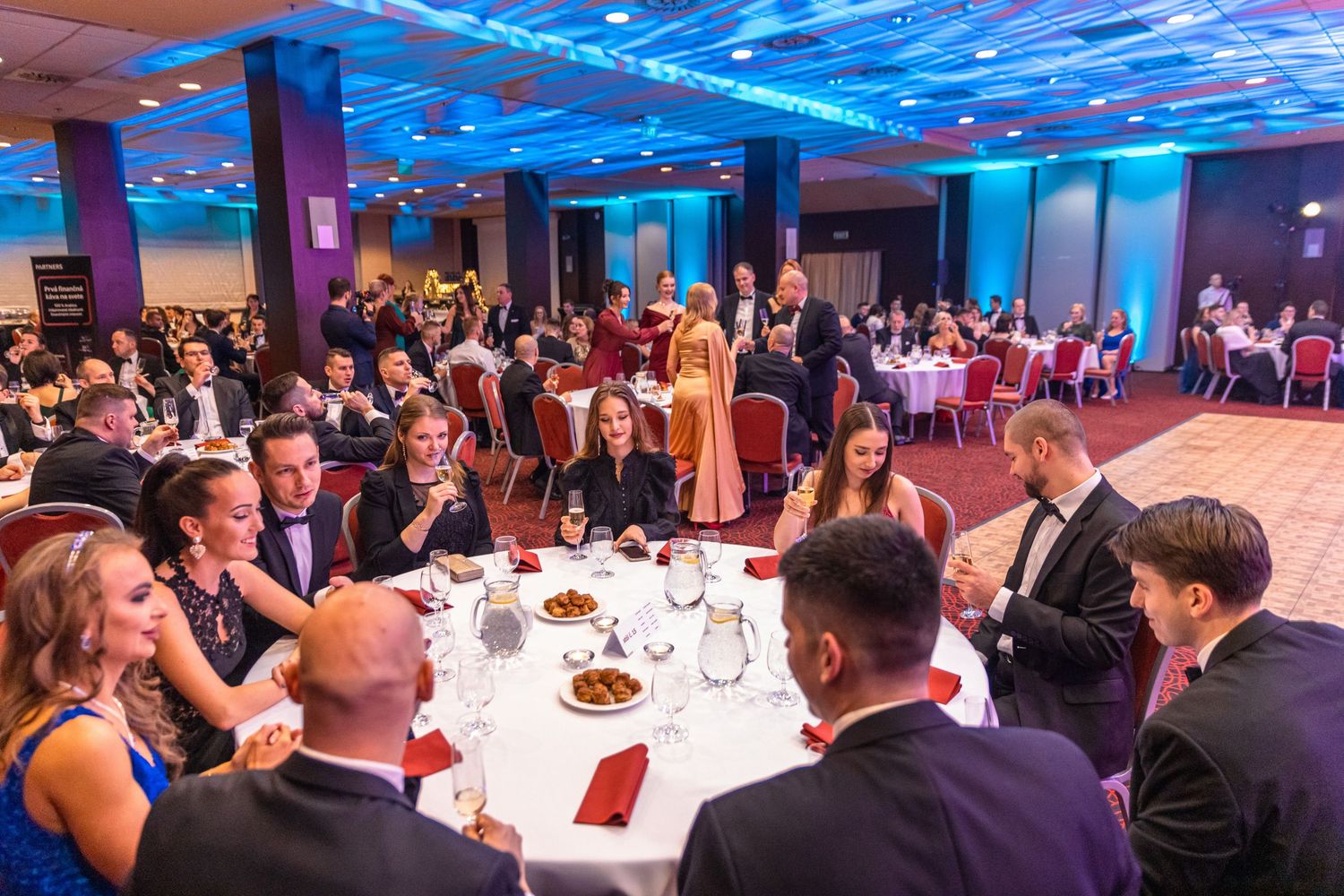 Corporate event space with blue uplighting and round tables set for a formal dinner gathering.