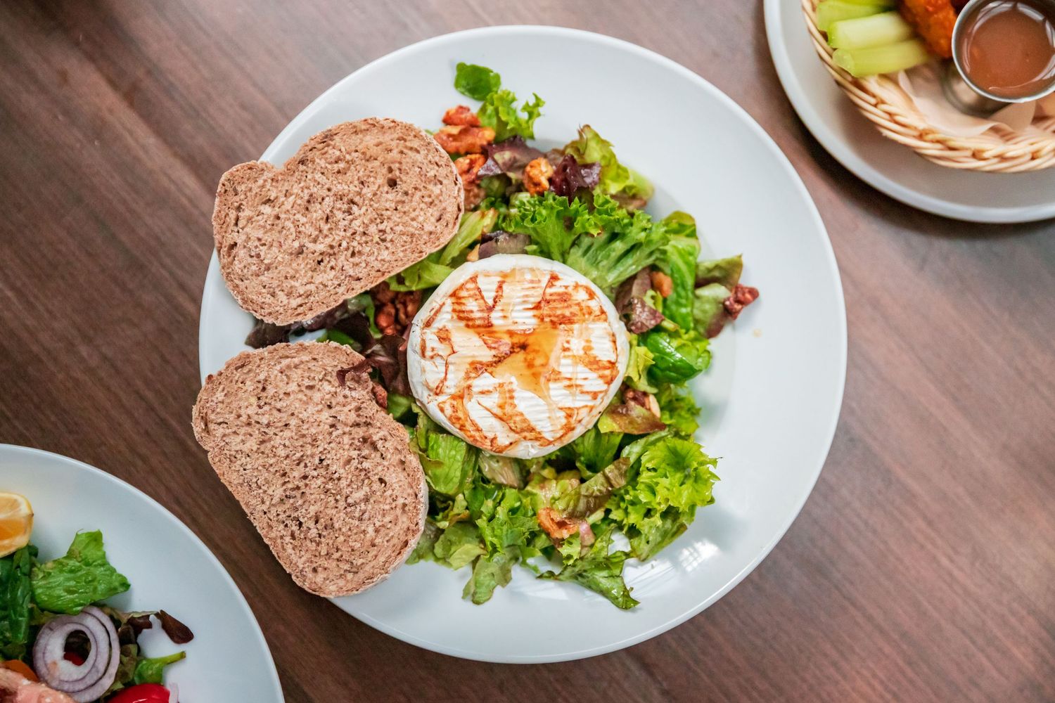 Various salad plates with fresh vegetables and bread served on white dishes.