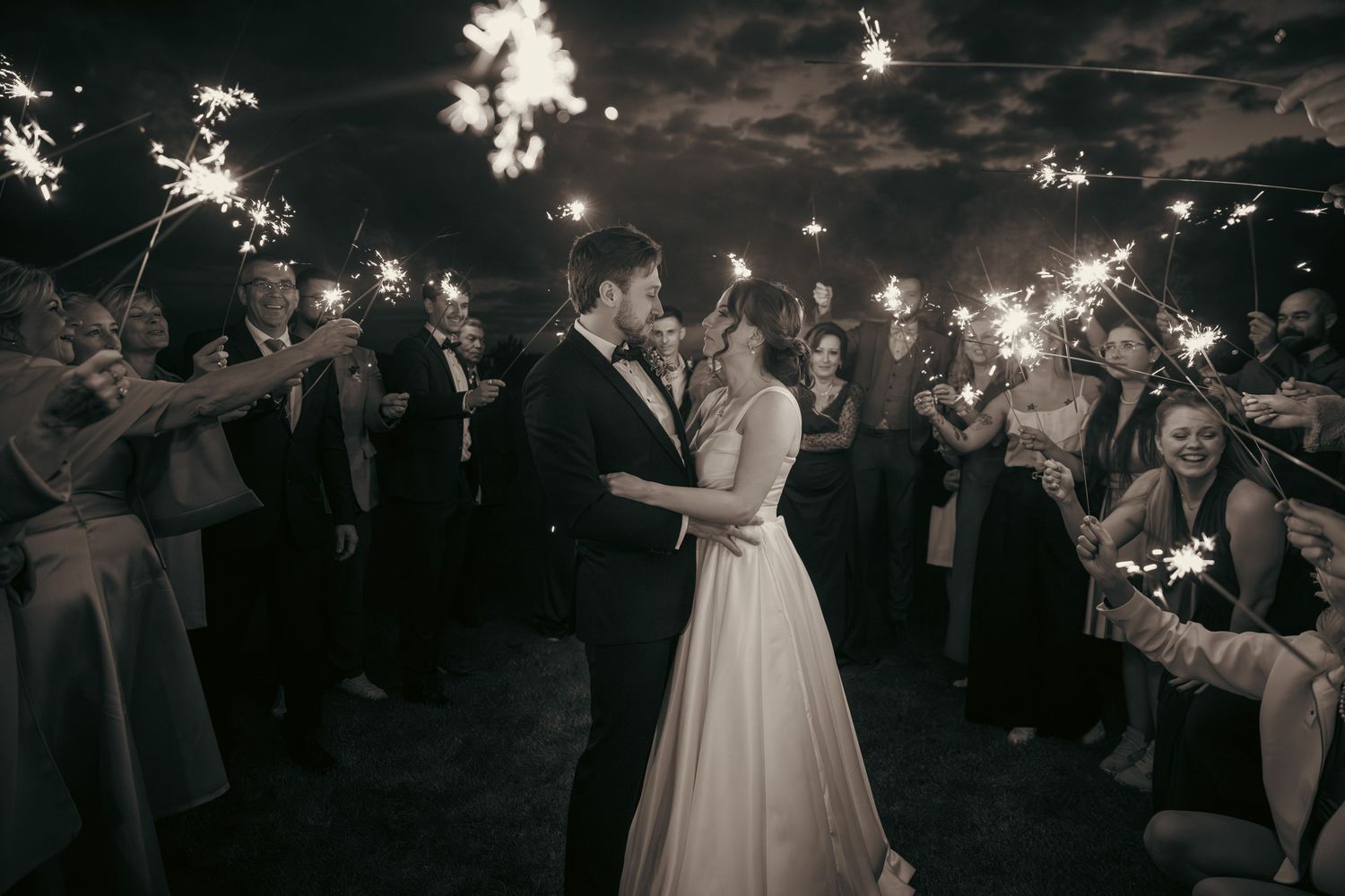 Wedding couple dances surrounded by guests holding sparklers at night.