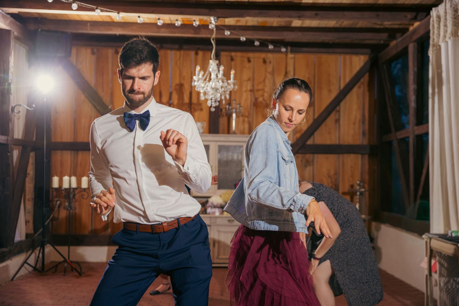 Wedding reception dance party in a rustic barn venue with string lights and wooden beams.