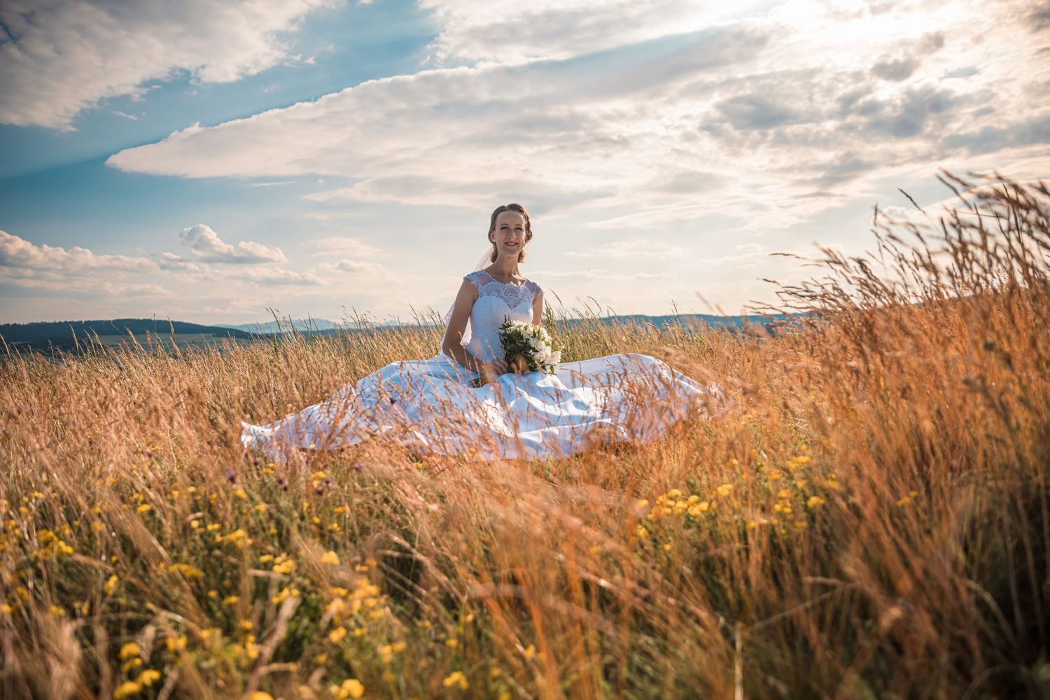 Wedding couple poses in golden wheat field against dramatic sky during sunset.