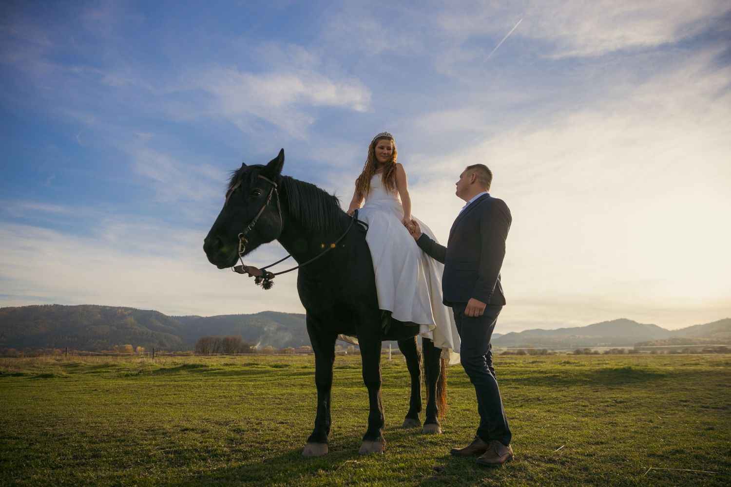 Scenic countryside photoshoot with horse and flowing white dress at sunset.