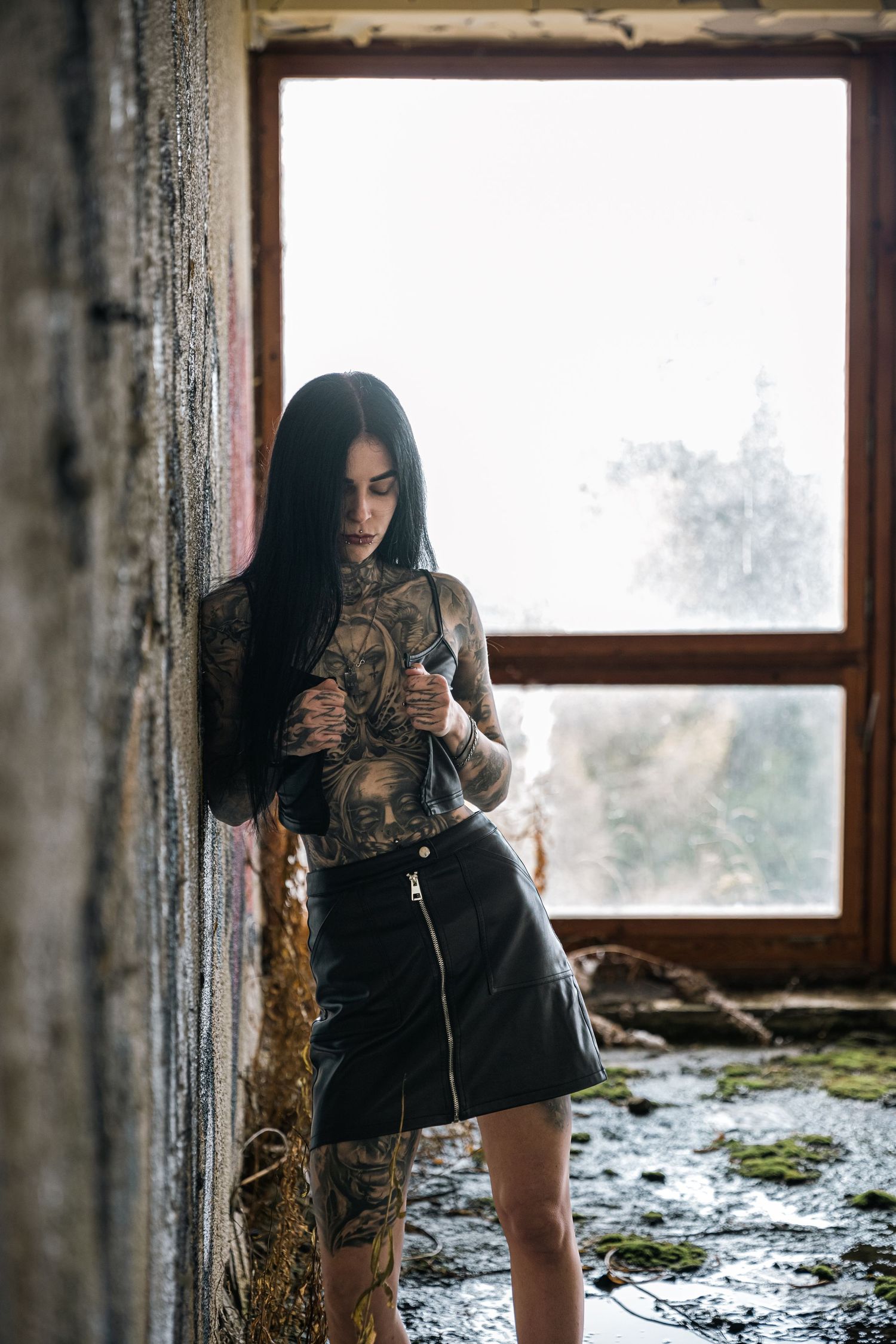 A figure in black clothing poses near a window in an abandoned building with snow visible outside.