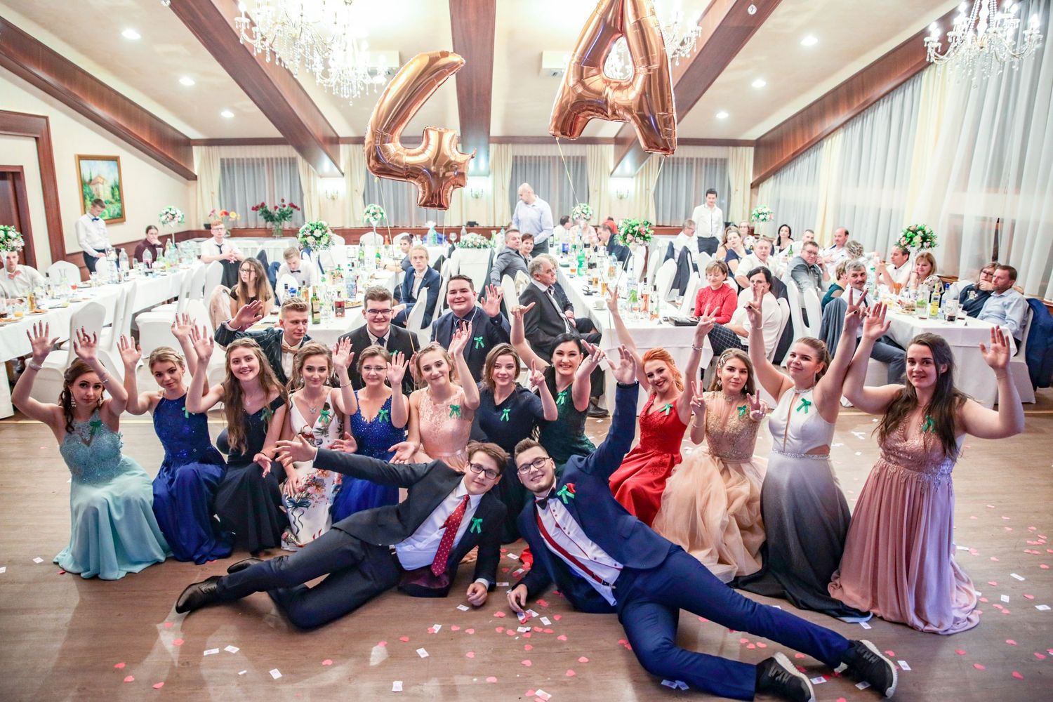 Large group photo of wedding guests arranged in panoramic formation in elegant ballroom.