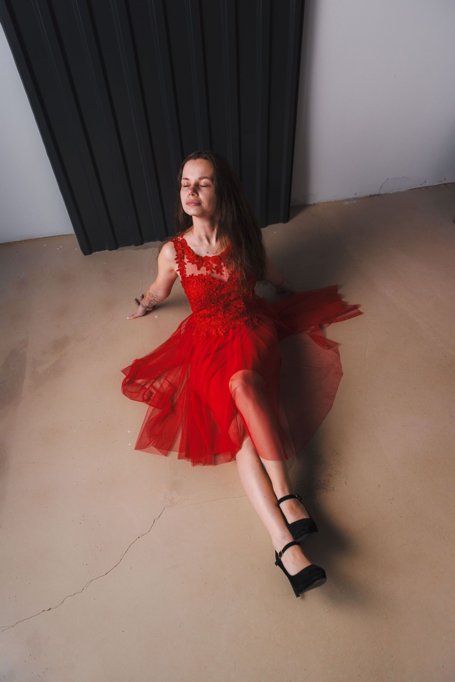 Model in flowing red dress reclines on floor in studio photoshoot.