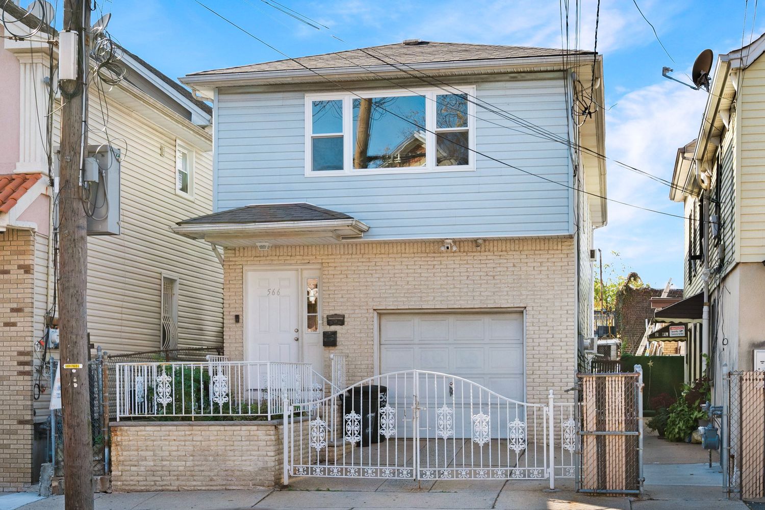 Exterior photo of front of two-story multi-family home, featuring front door, garage, large window, brick and siding, and blue sky.