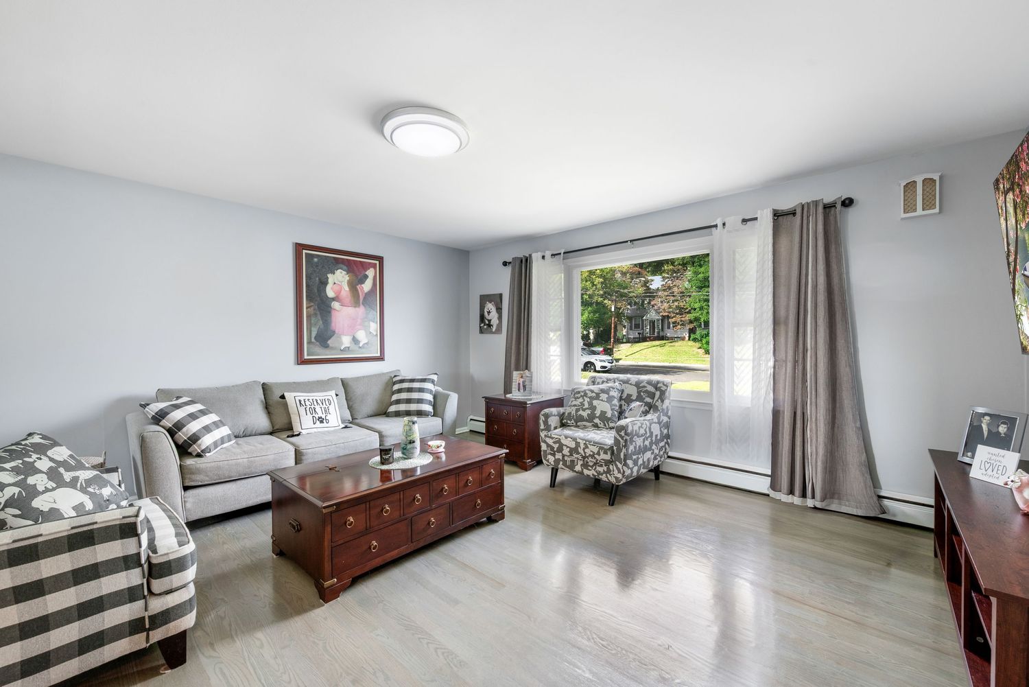 A living room with gray walls features a sofa, two checkered armchairs, a wooden coffee table, a TV on a stand, artwork on the walls