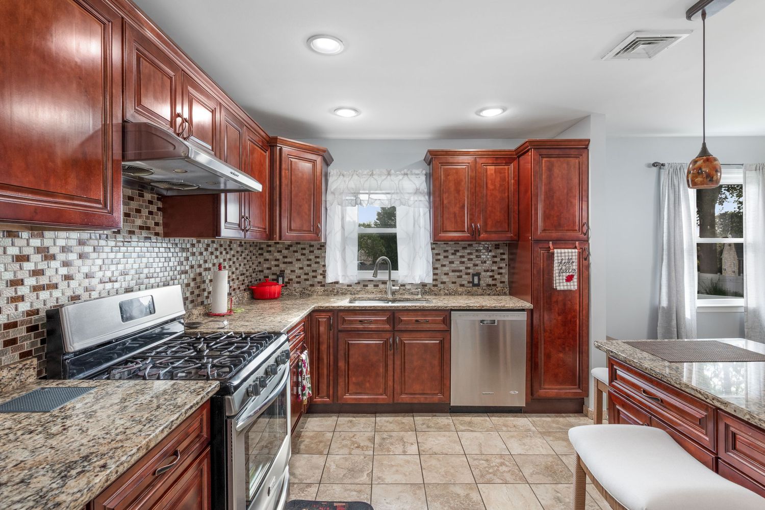 Kitchen with cherry wood cabinets, tile backsplash and floors, quartz countertops, featuring stainless steel oven and dish washer.