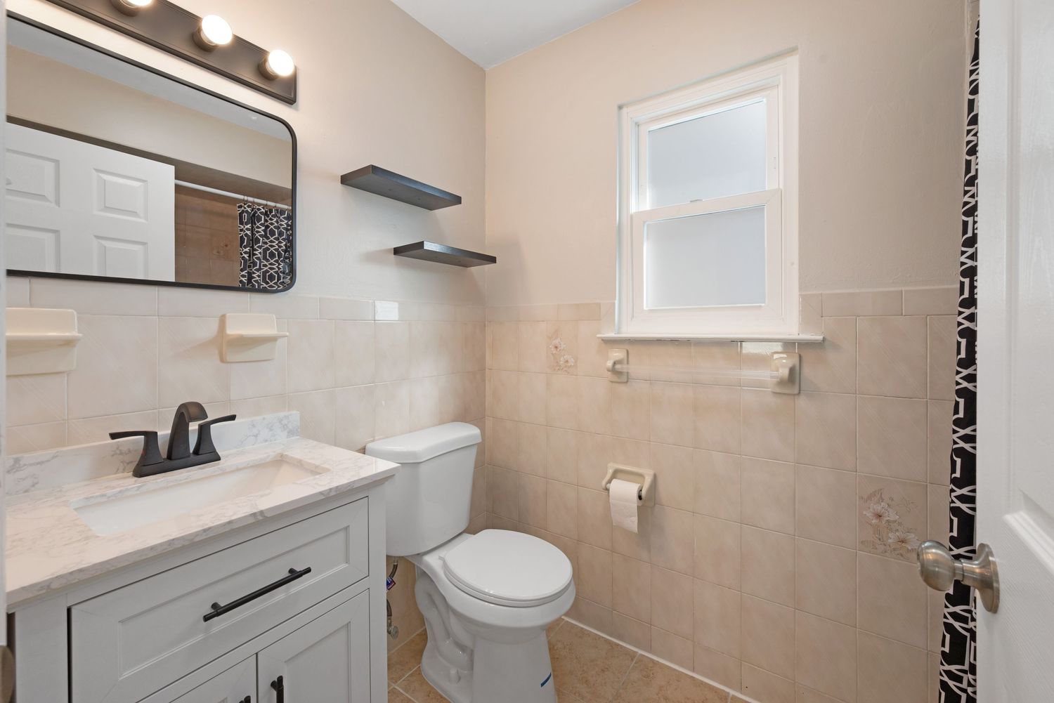 Updated bathrooom with window featuring sink, mirror, and toilet.