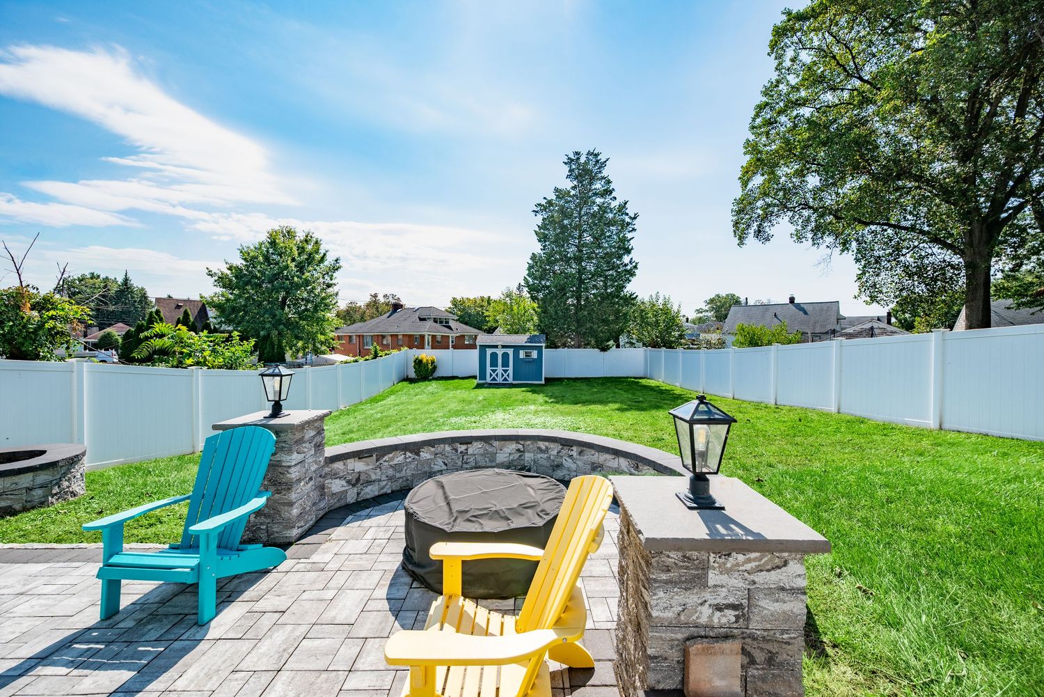 Large backyard with green grass, blue sky, a fire pit, and patio furnature.