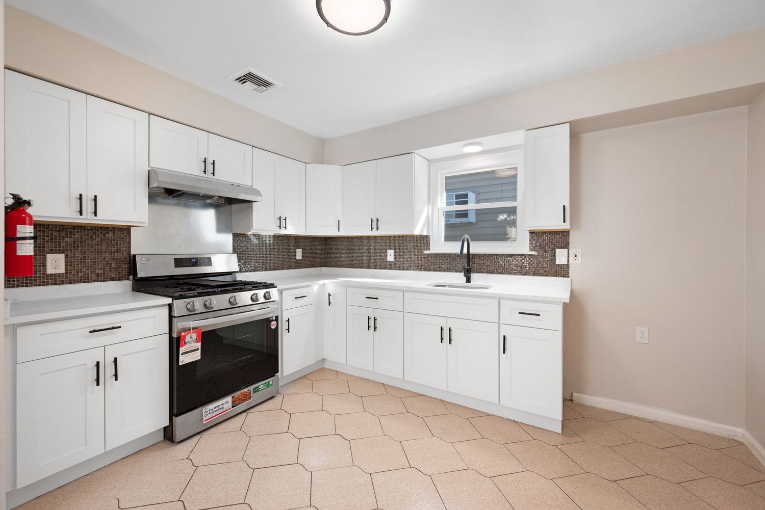 Renovated kitchen featuring a new stove, white cabinets and counters, window over the sink, and space for a refrigerator.