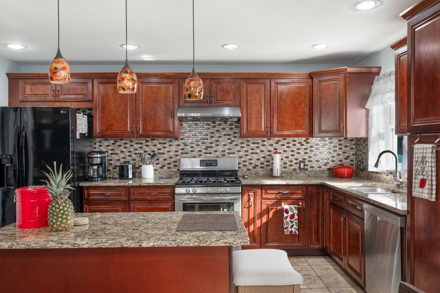 Beautiful kitchen with cherry wood cabinets, tile backsplash and floors, quartz countertops, featuring stainless steel oven and dish washer.