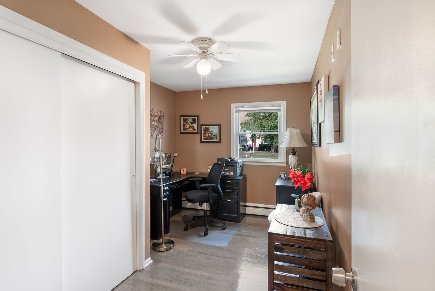 Office with tan walls and window featuring a desk and chair, a closet and overhead light.