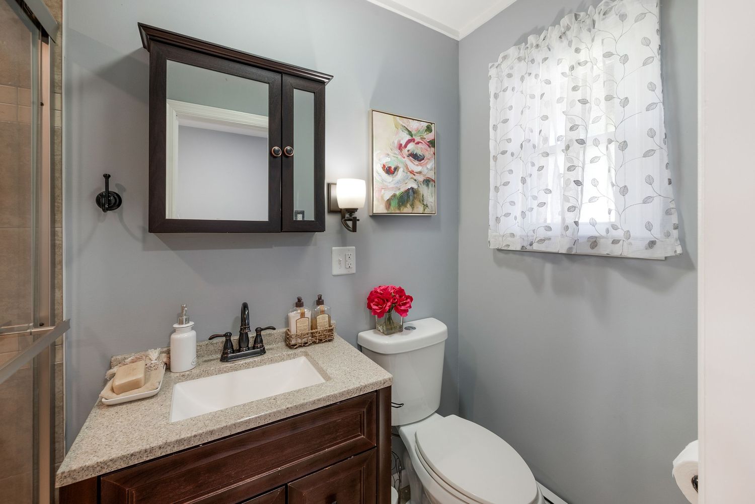 Small bathroom with sink, shower, toilet and window.
