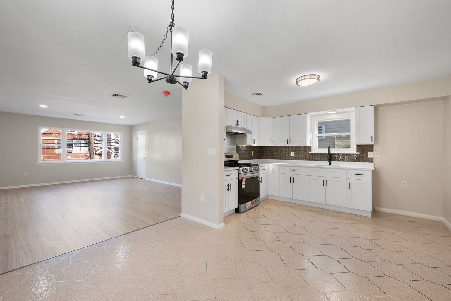 Spacious open layout of dining room and kitchen with tile floors and a living room with large window and hardwood floors and beige walls.