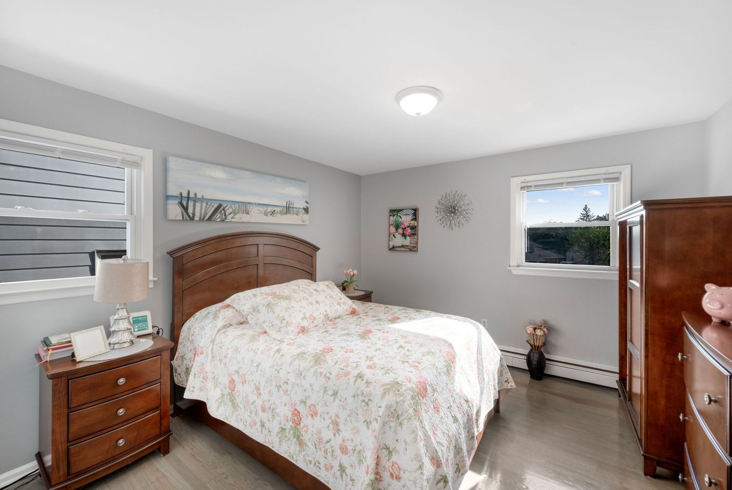 Master bedroom with grey walls, two windows, and hardwood floors featuring matching cherry wood bed, side tables, and dresser.